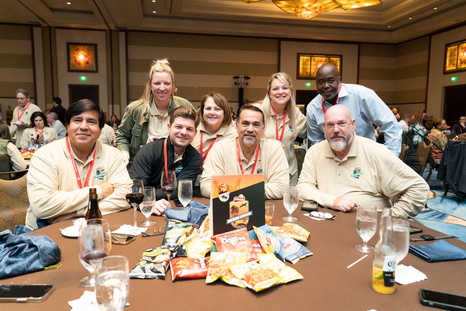 Group of colleagues smiling at a conference banquet table with snacks, drinks, and event materials displayed.