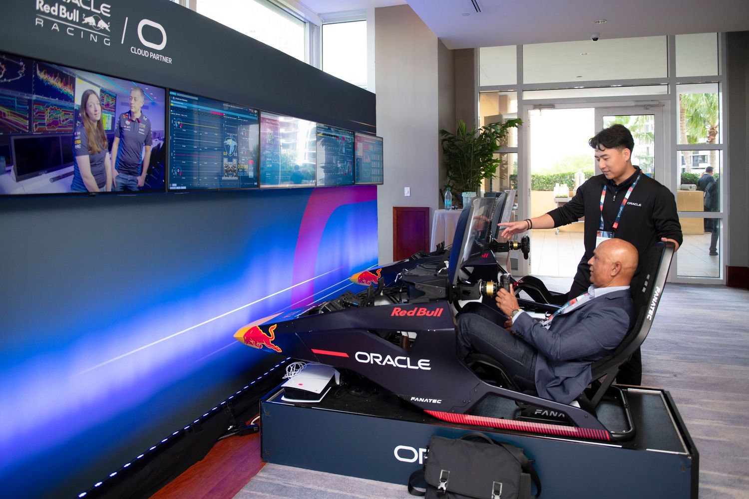 Two men using an Oracle Red Bull Racing F1 simulator setup with large curved screens at a technology event.