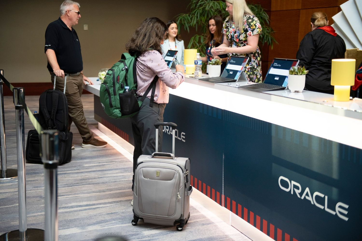 People checking in at an Oracle conference registration desk with luggage in a modern convention center.