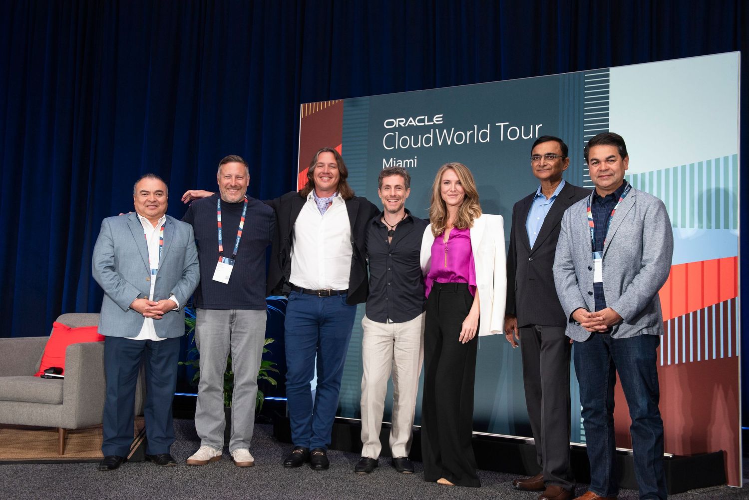 Seven professionals pose together at Oracle CloudWorld Tour Miami event in front of branded backdrop.