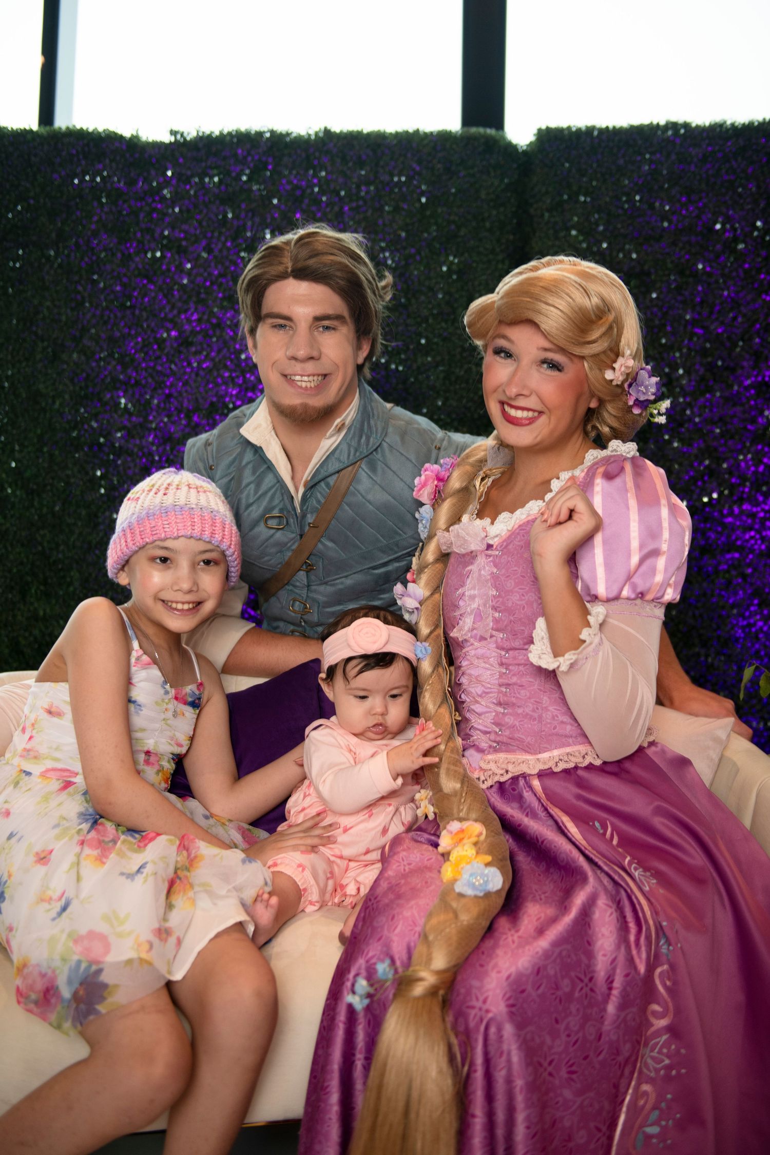 Family poses with Rapunzel and Flynn Rider Disney characters at a themed event, including two young girls.