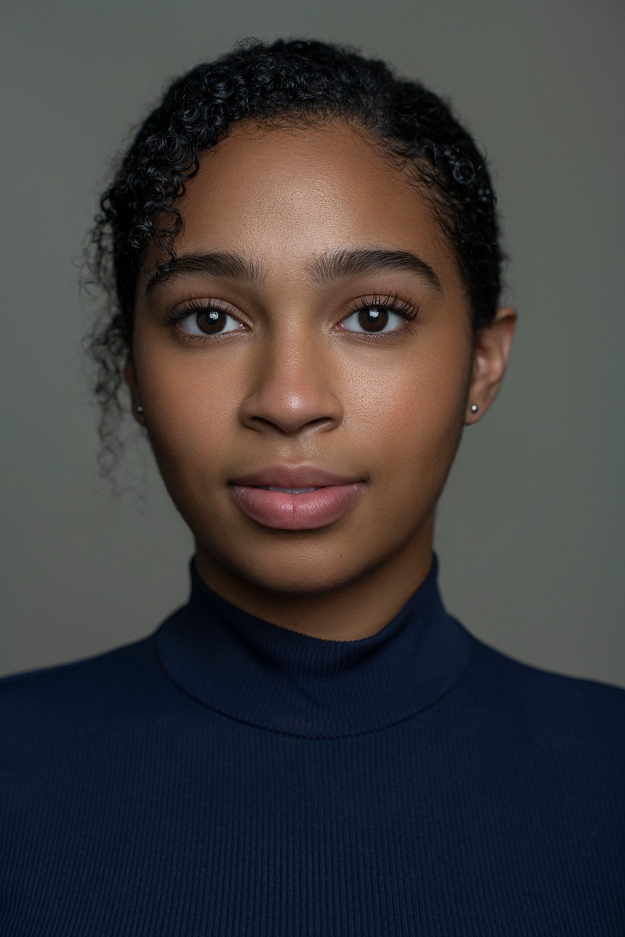Young Black woman with curly updo wearing a navy turtleneck against a gray background.