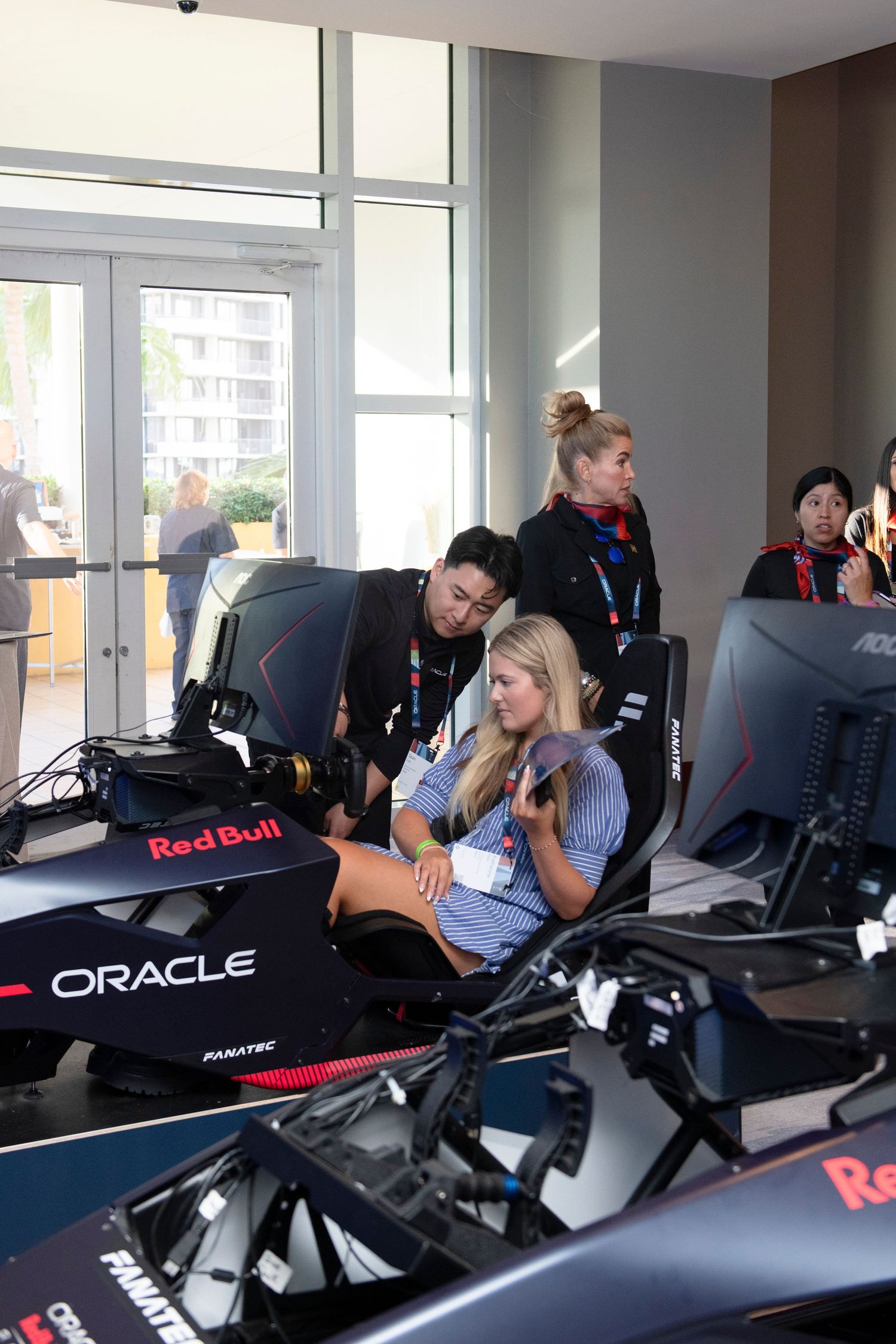 Woman tries Oracle Red Bull Racing F1 simulator with staff assistance at an indoor motorsport event.