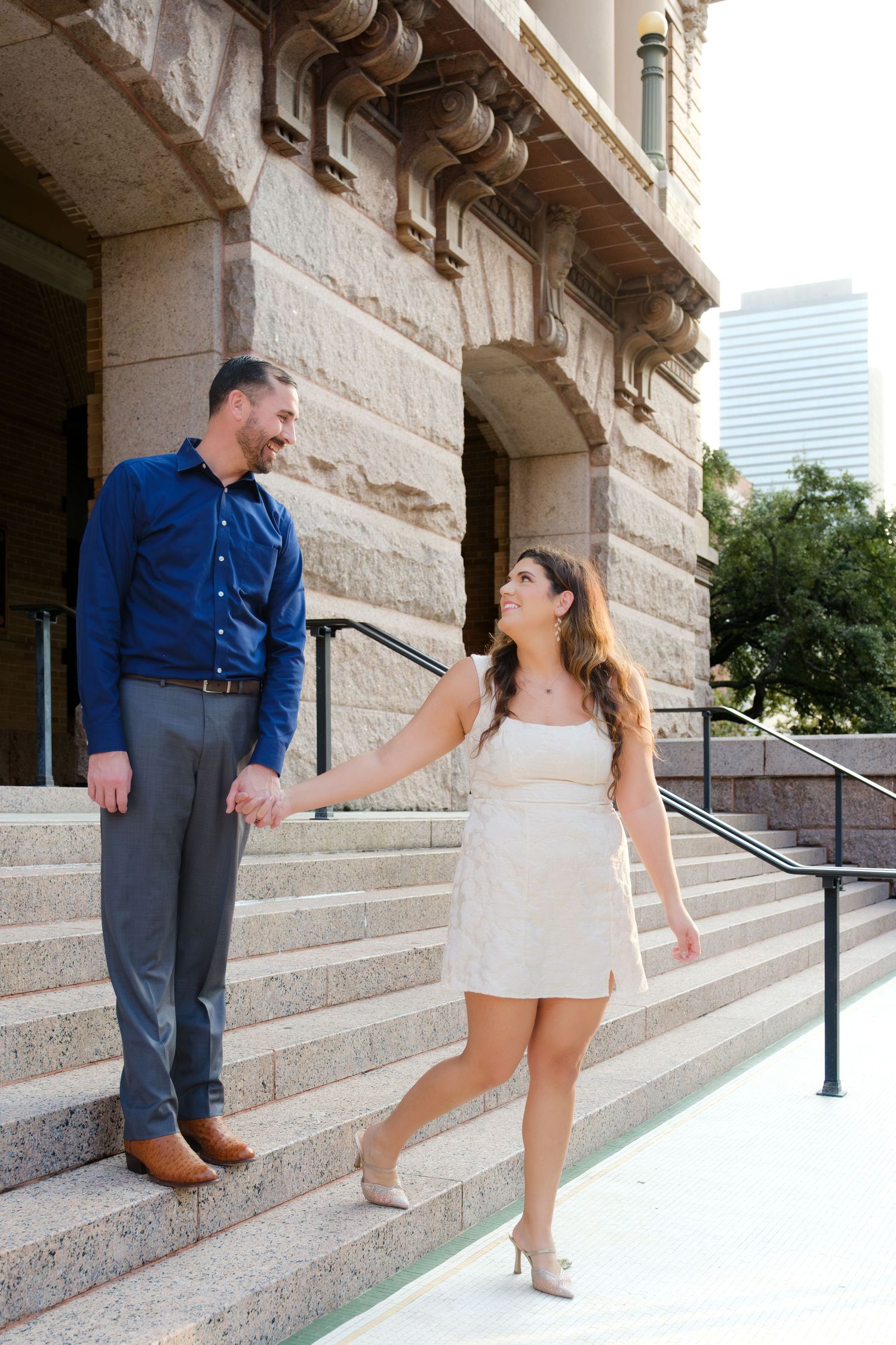 Couple walks down stairs holding hands at courthouse in Houston, Tx during engagement session.