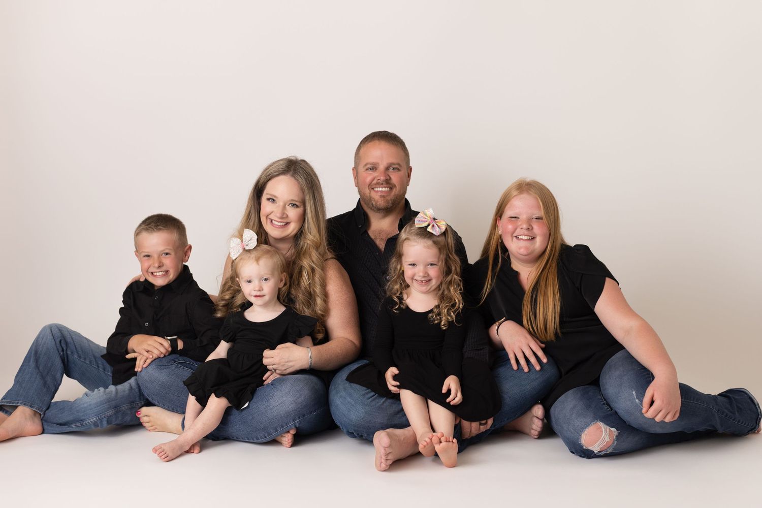 Family of six in matching black outfits sitting together and smiling in a studio portrait. Family Photographer East Texas
