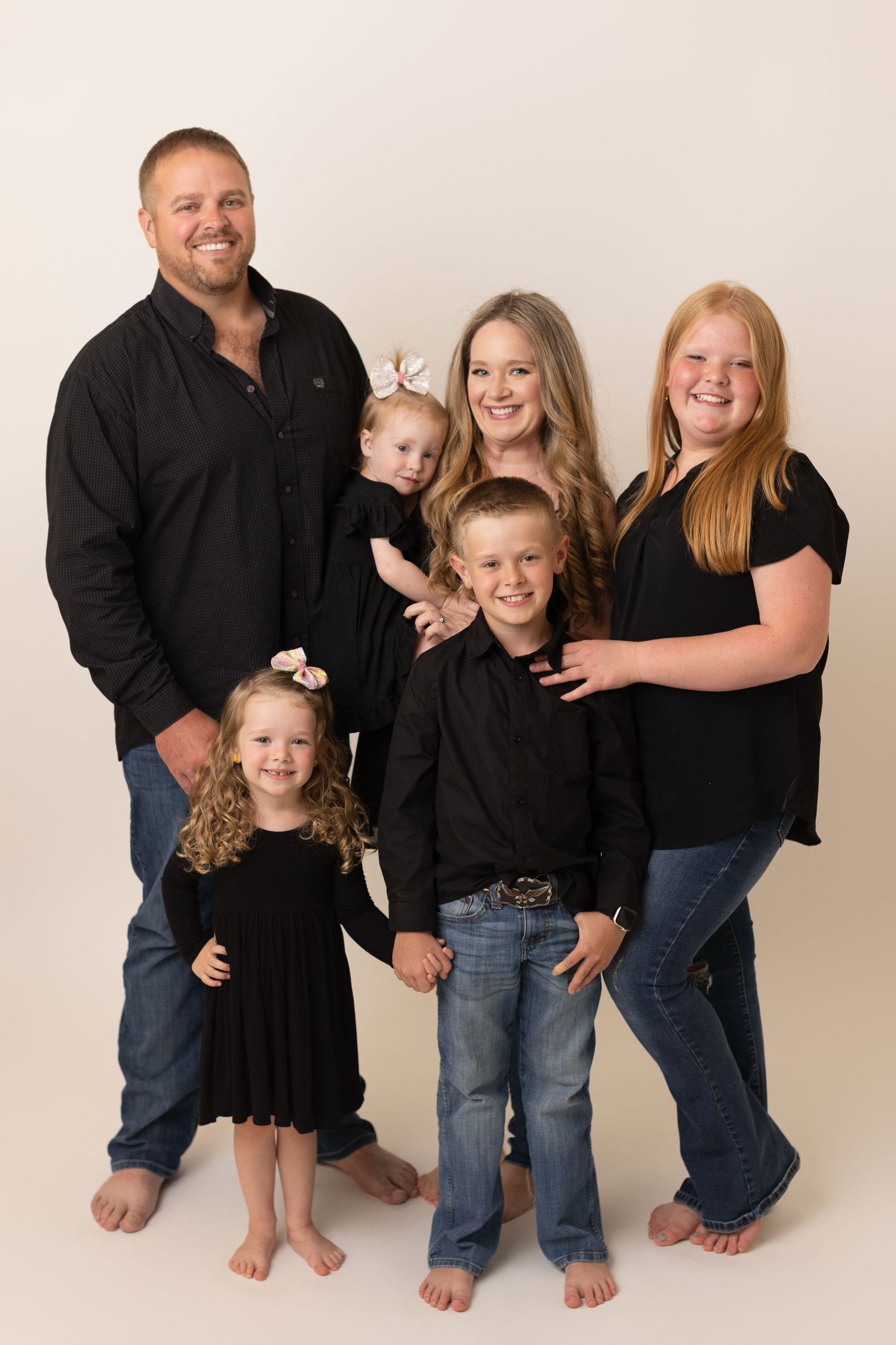 Family of six dressed in matching black outfits posing together barefoot during a studio family portrait session. Family Photographer