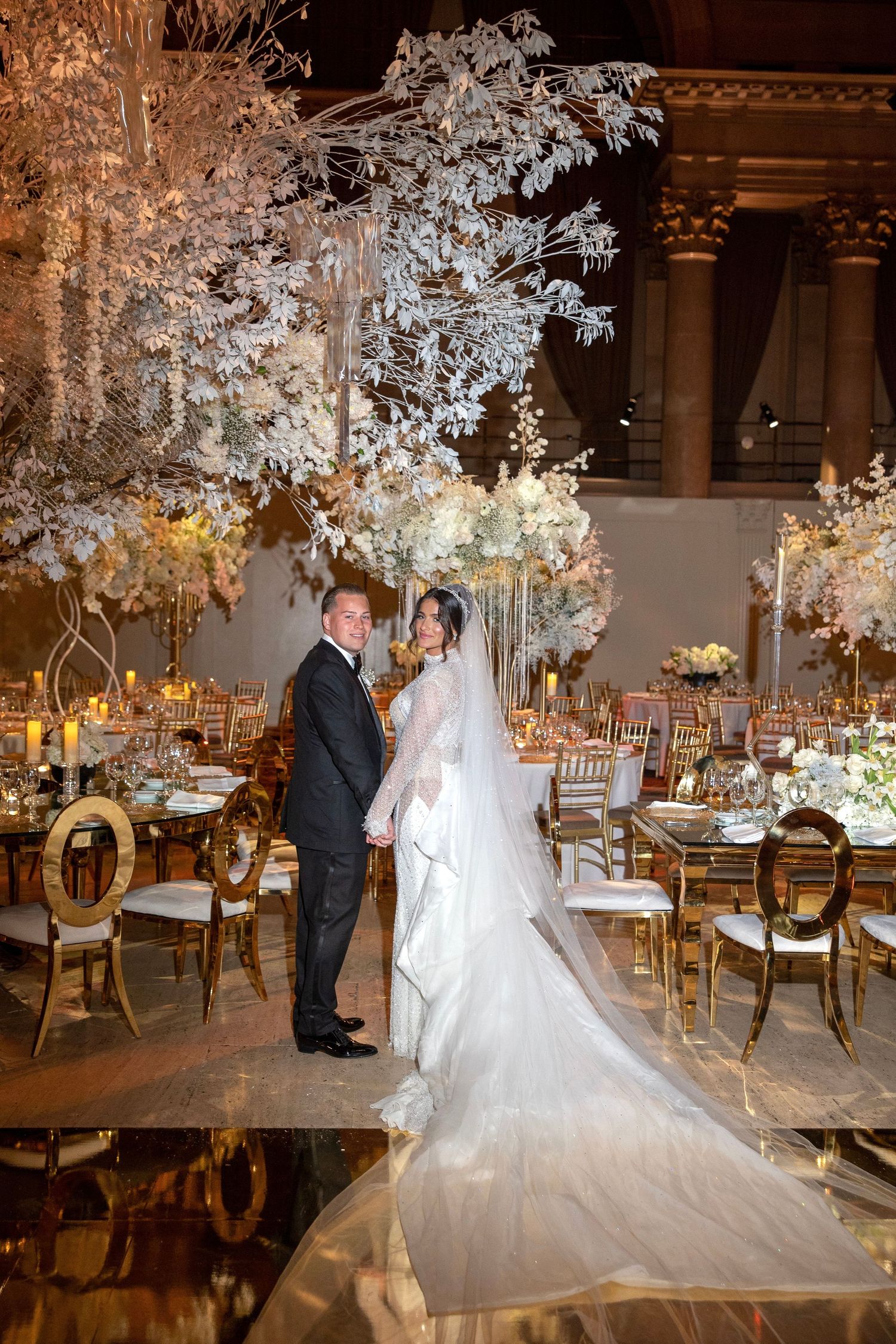 Wedding reception venue with dramatic white floral arrangements and elegant table settings.