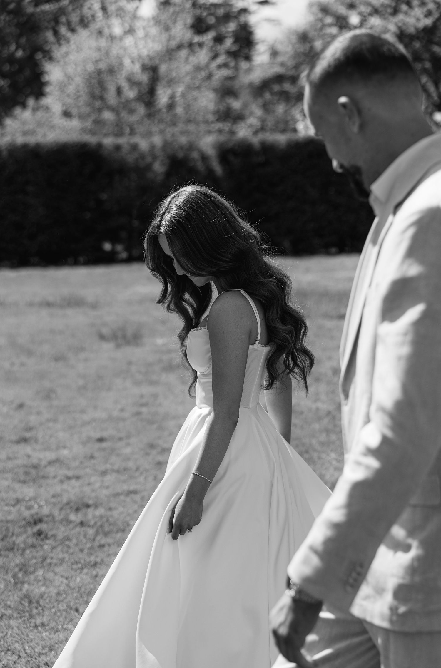 Black and white photo of bride in flowing white dress and groom walking outdoors during outdoor wedding photoshoot.