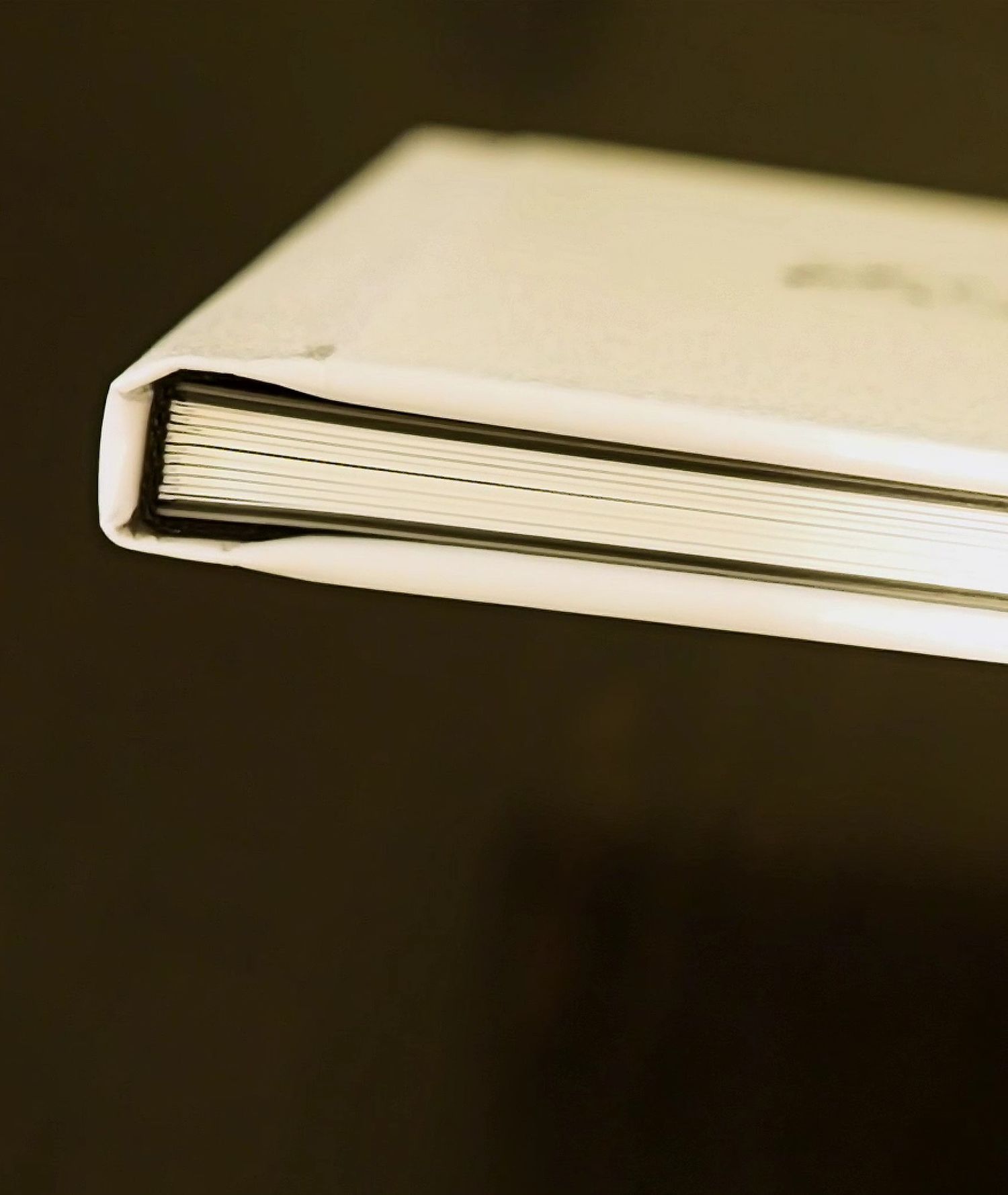 Close-up of a white hardcover photo album showing its thick pages against a dark background.