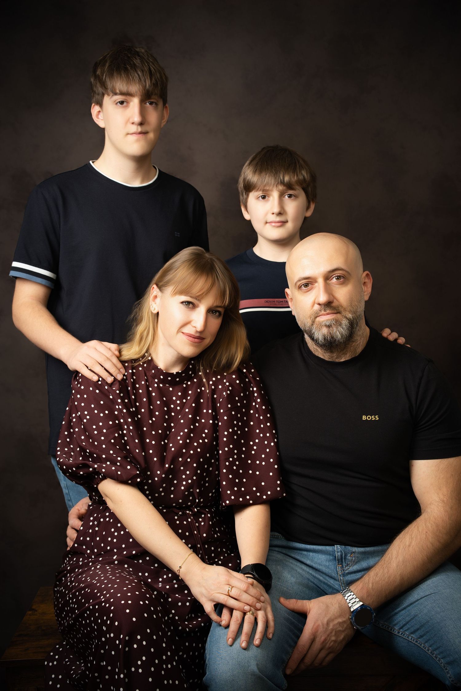 A family portrait with a seated woman in a polka dot dress, a bearded man, and two boys standing behind them in a studio.