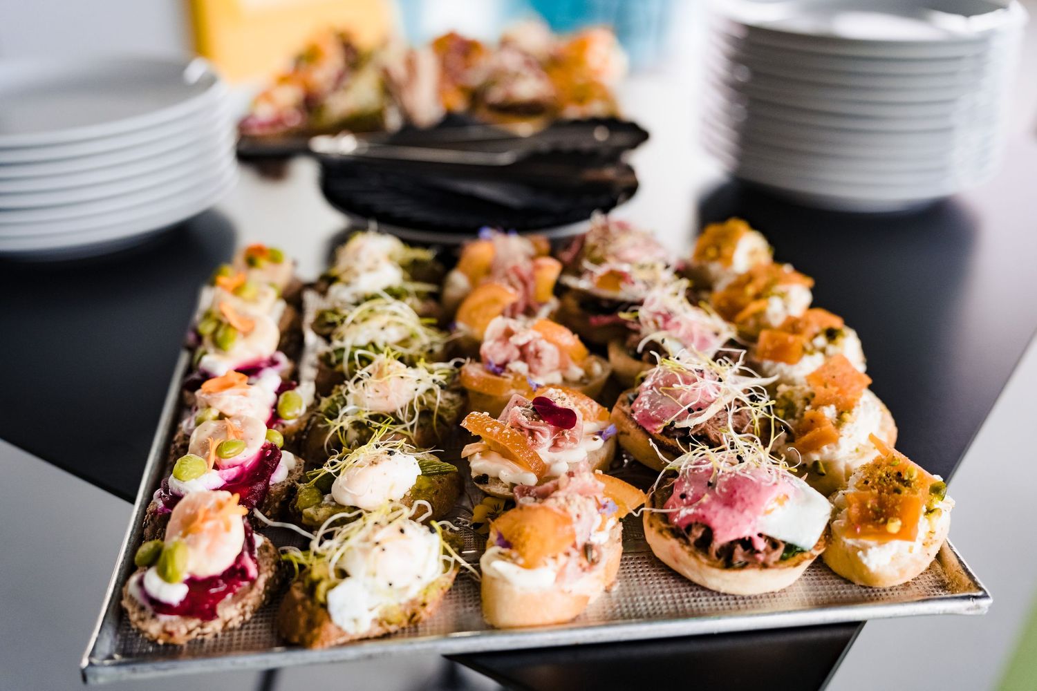 Tray of assorted open-faced canapés topped with fish, cream cheese, sprouts and garnishes, served at a company event.