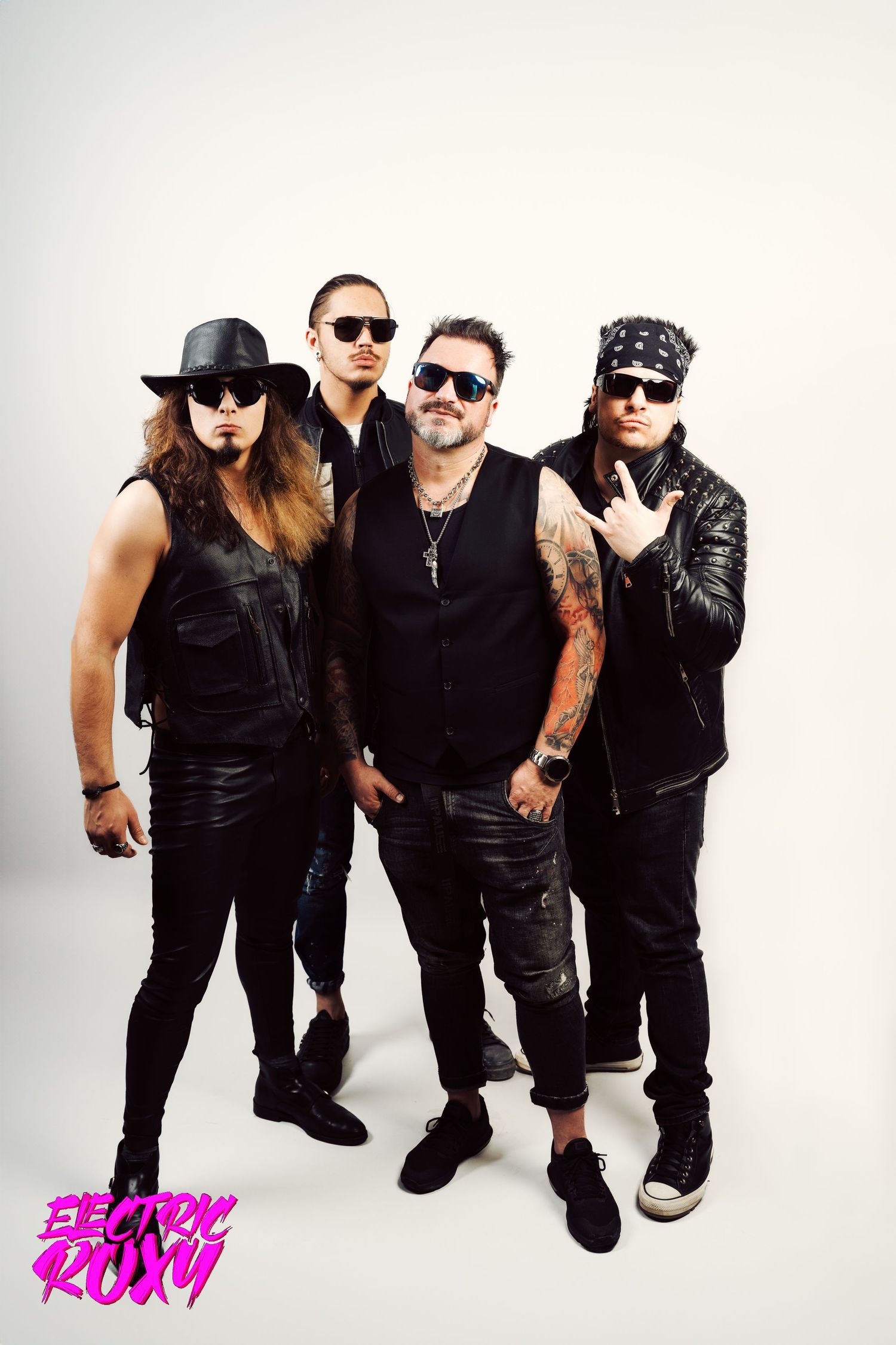 Electric Roxy rock band stands in a group against a white background, wearing black leather, sunglasses, a hat and a bandana.