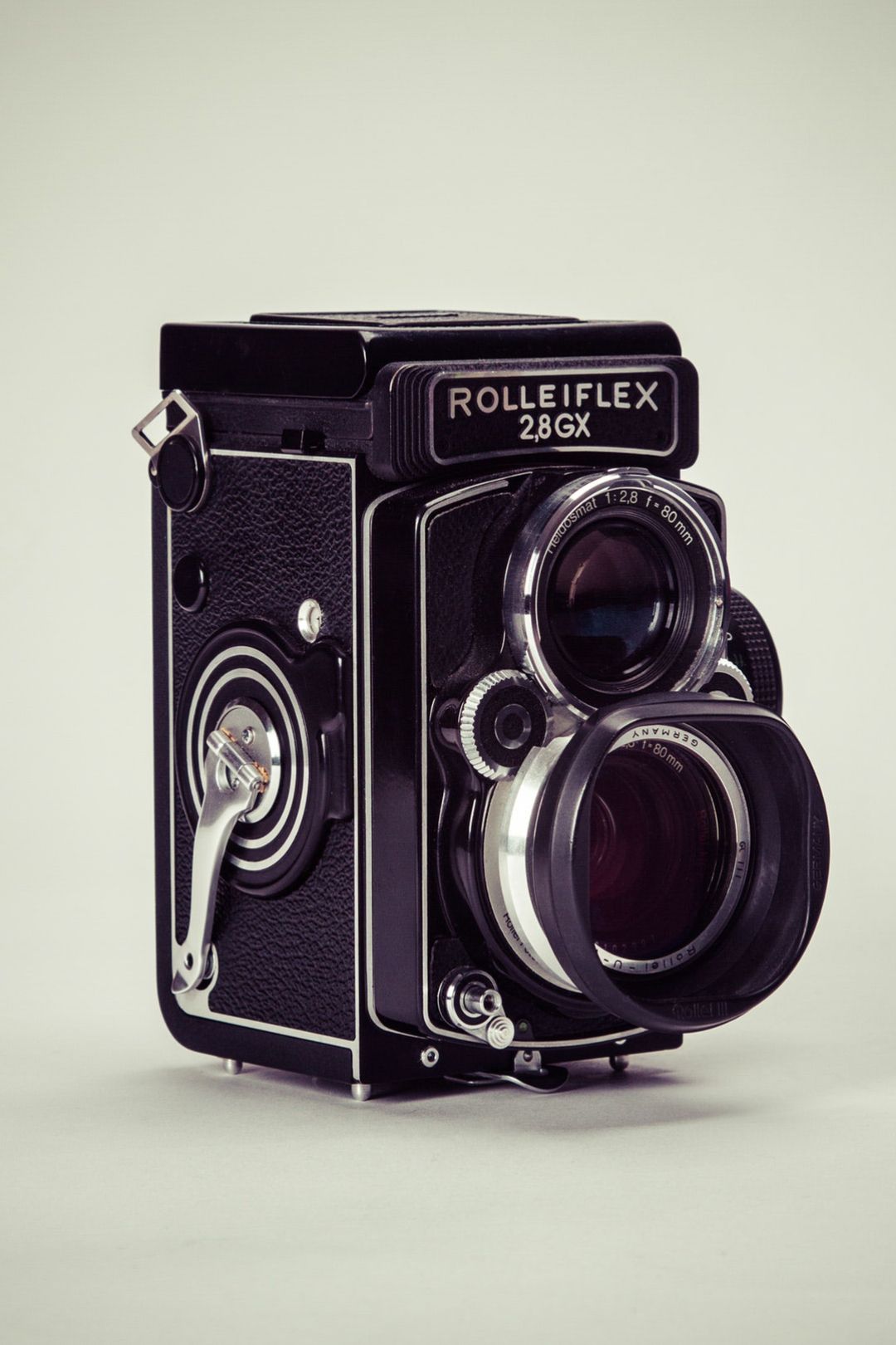 Vintage black Rolleiflex 2.8GX twin-lens reflex camera with a lens hood photographed against a soft gray background.