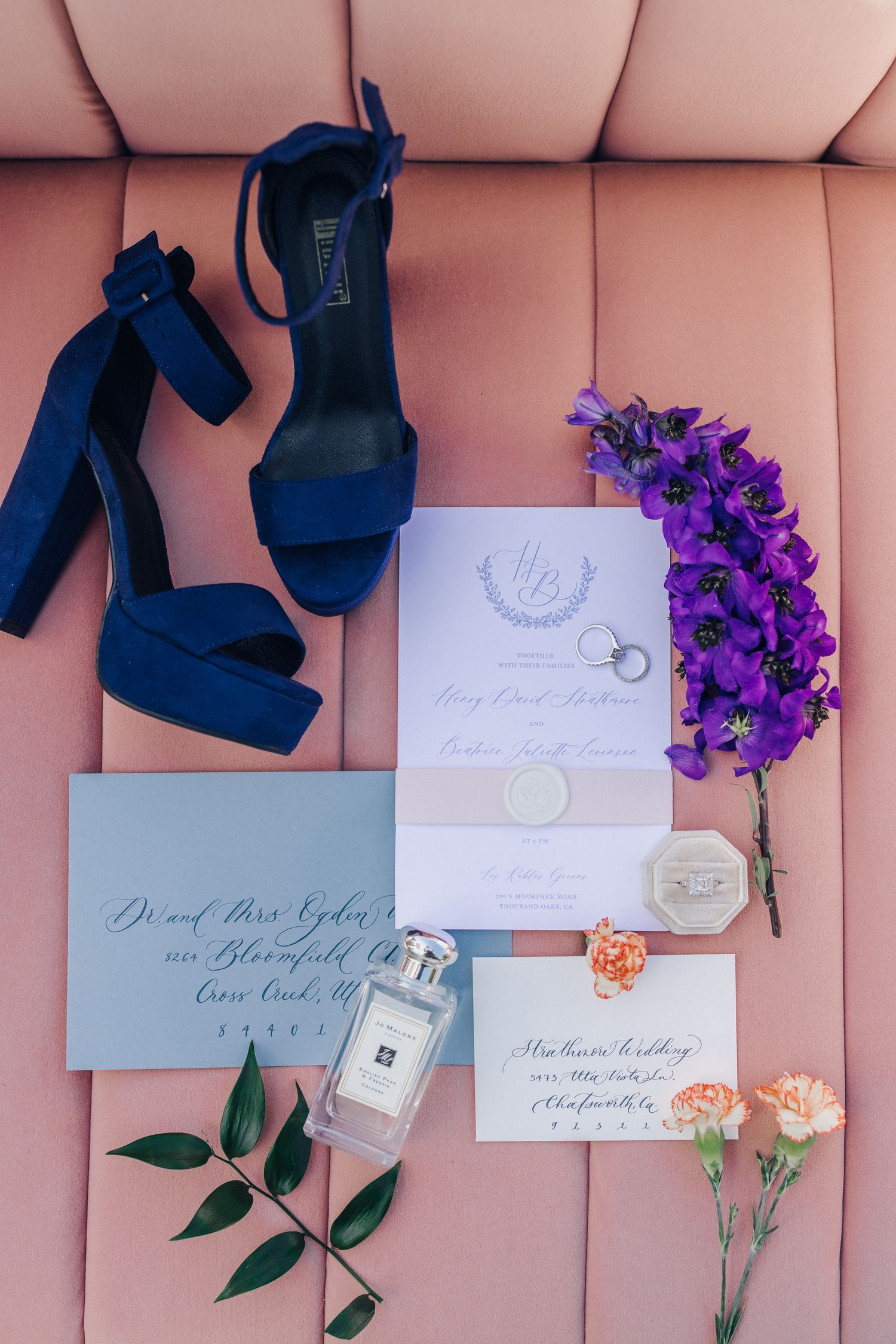 Blue high heel shoes, blue stationery, and Jo Malone perfume with flowers on a pink velvet sofa before an estate wedding in Newport, RI