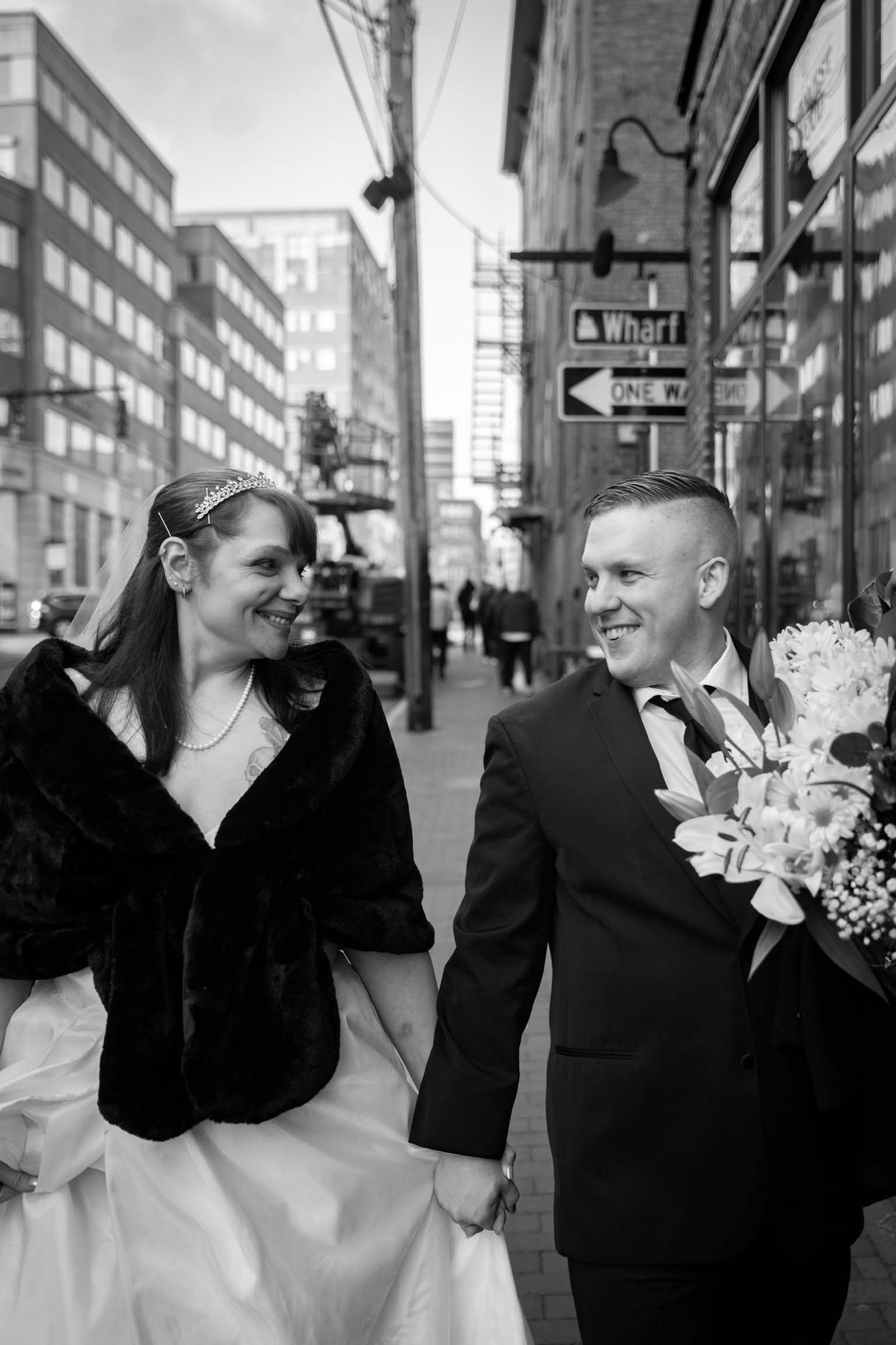Bride and groom hold hands and stroll the city streets at their glamorous Winter Christmas wedding in the Old Port, Portland, Maine