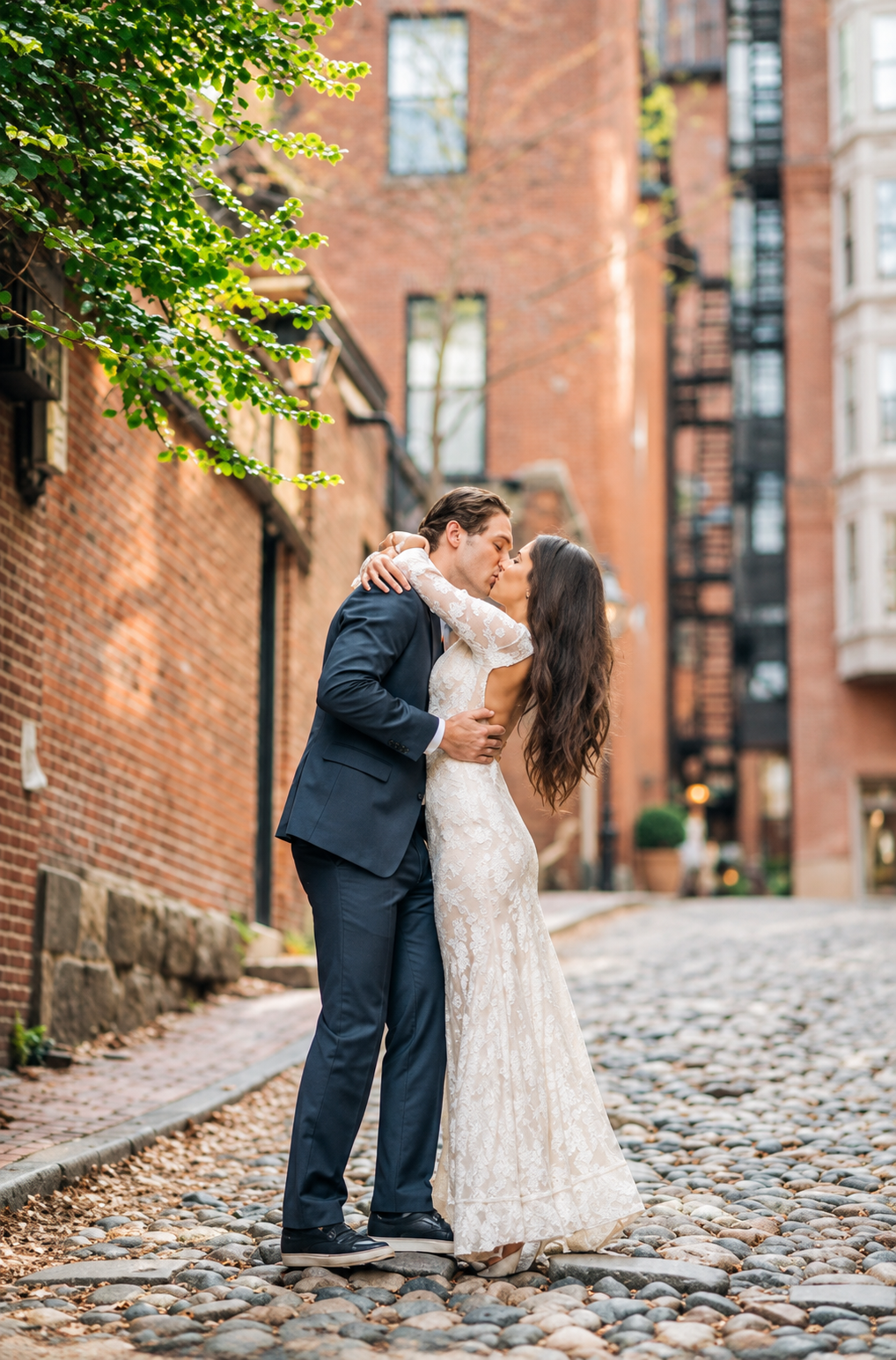 Bride and groom share a kiss on a cobblestone street surrounded by historic buildings at their classic Italian North End Boston wedding