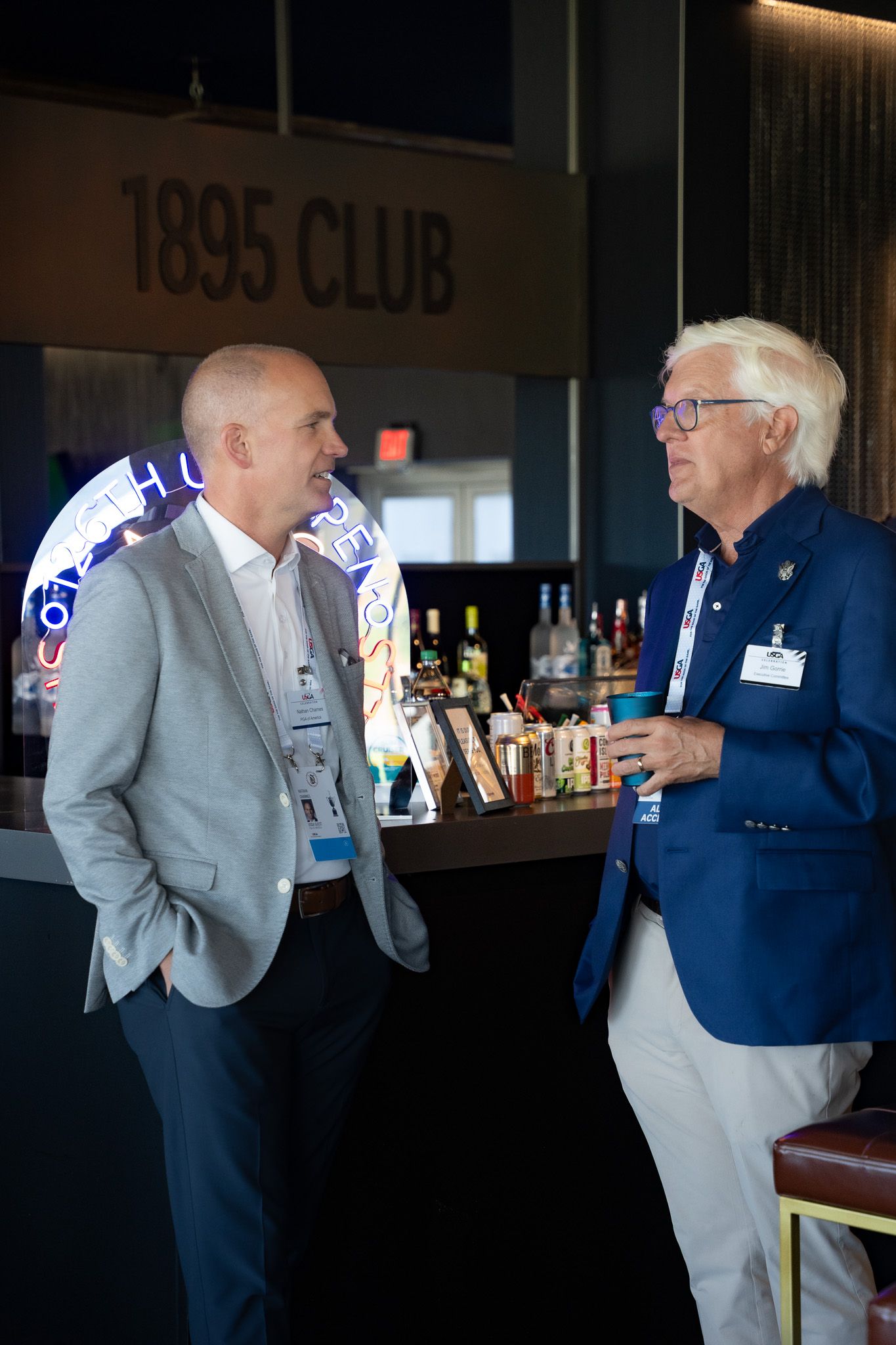Corporate event photography of two guests smiling at a bar during a party at the U.S. Open at Shinnecock Hills in the Hamptons, New York.