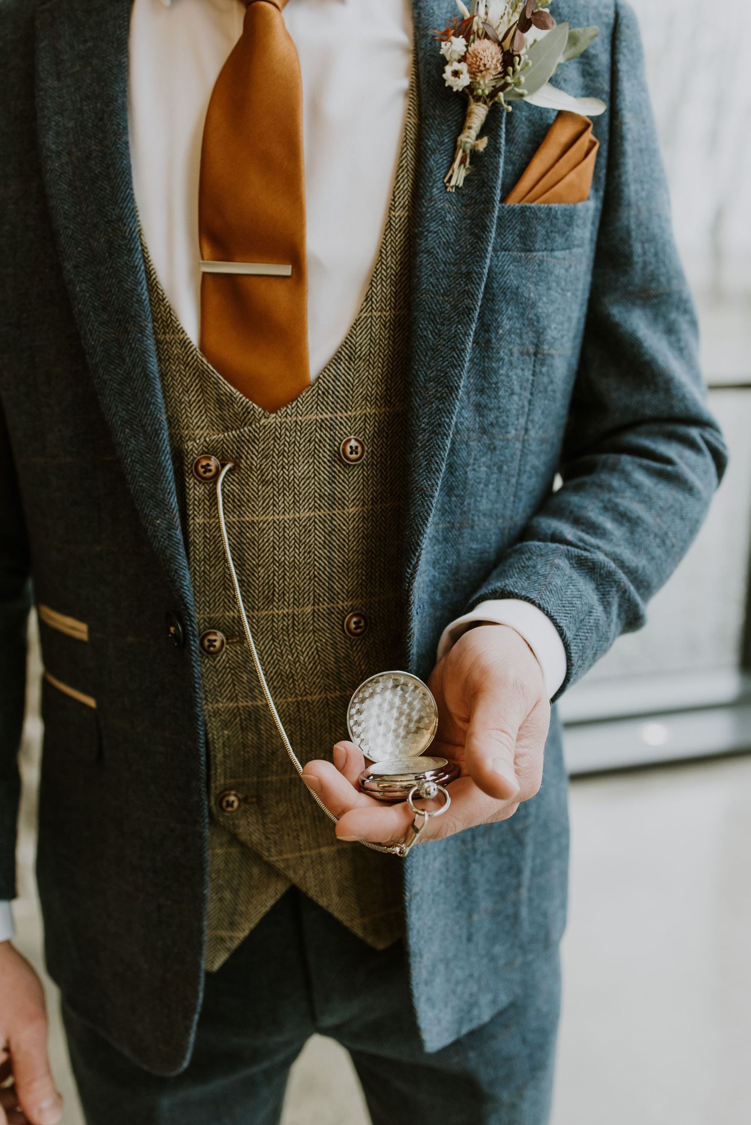 Smartly dressed groom holds an antique pocket watch on a chain before his estate wedding in Middleburg, Virginia