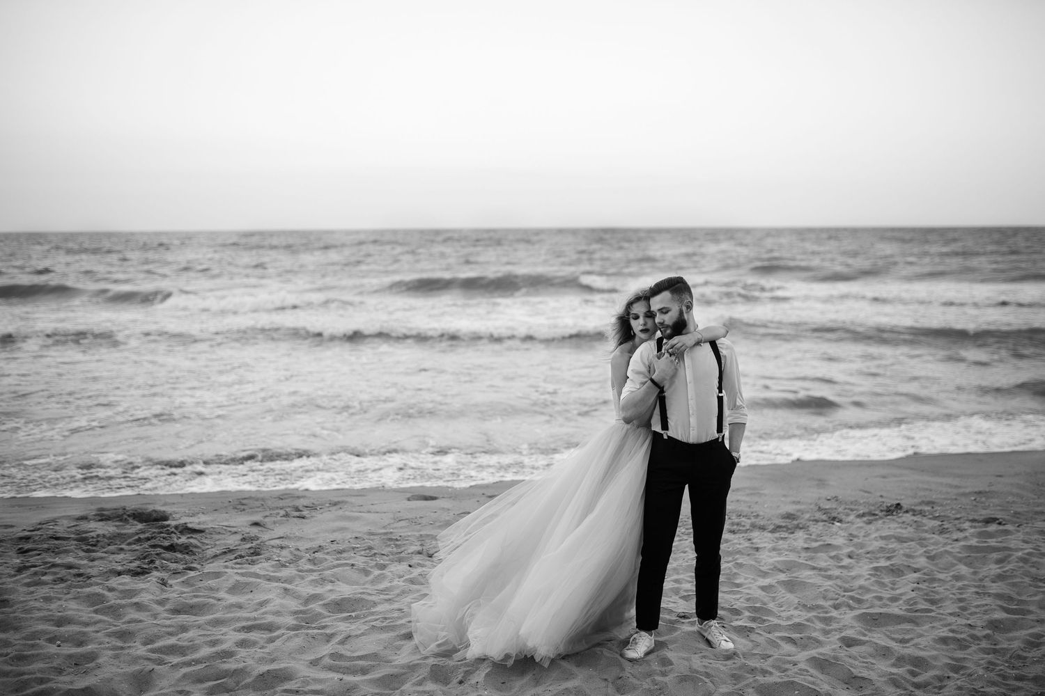 A bride's dress flows in the wind as she hugs her husband on the beach after their wedding ceremony in Newburyport, Massachusetts