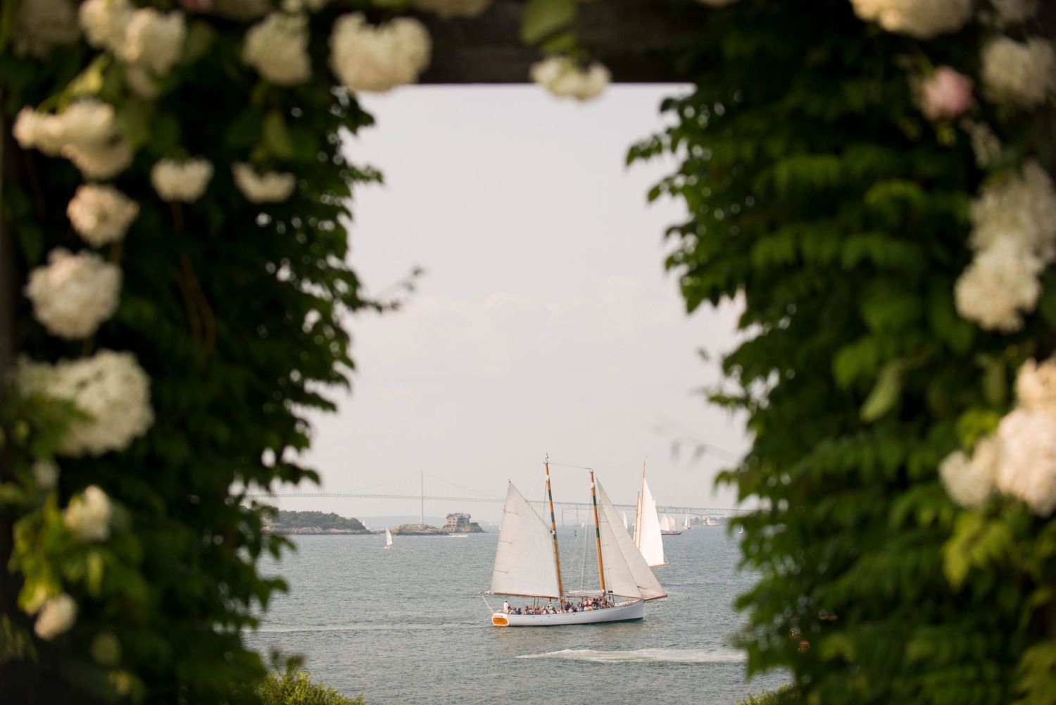 A sailboat passes through a floral archway before a luxury estate wedding in Newport, Rhode Island
