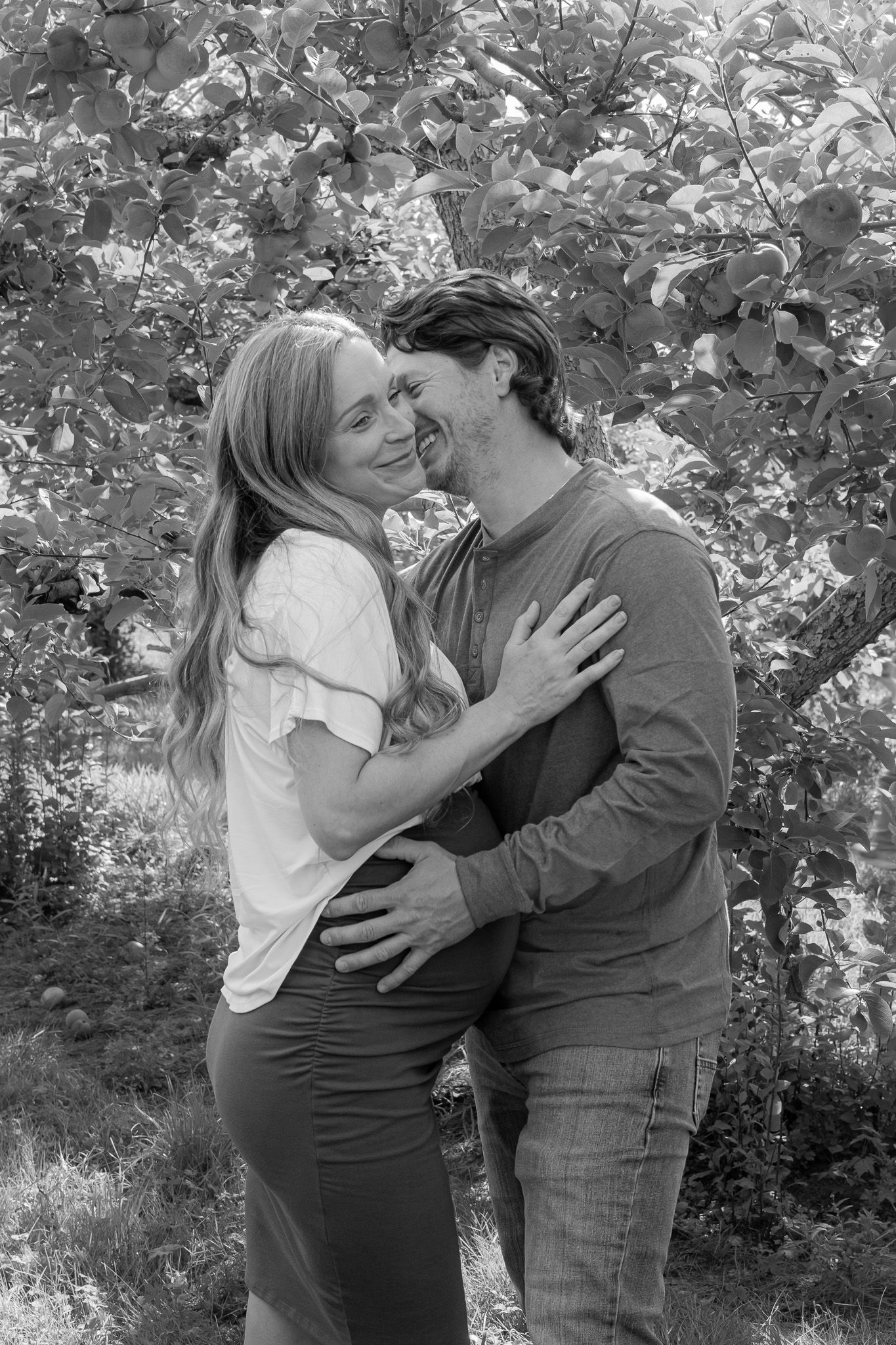 Family portrait of a husband kissing his wife and gently touching her pregnant belly at Applecrest Orchards in Hampton Falls, New Hampshire