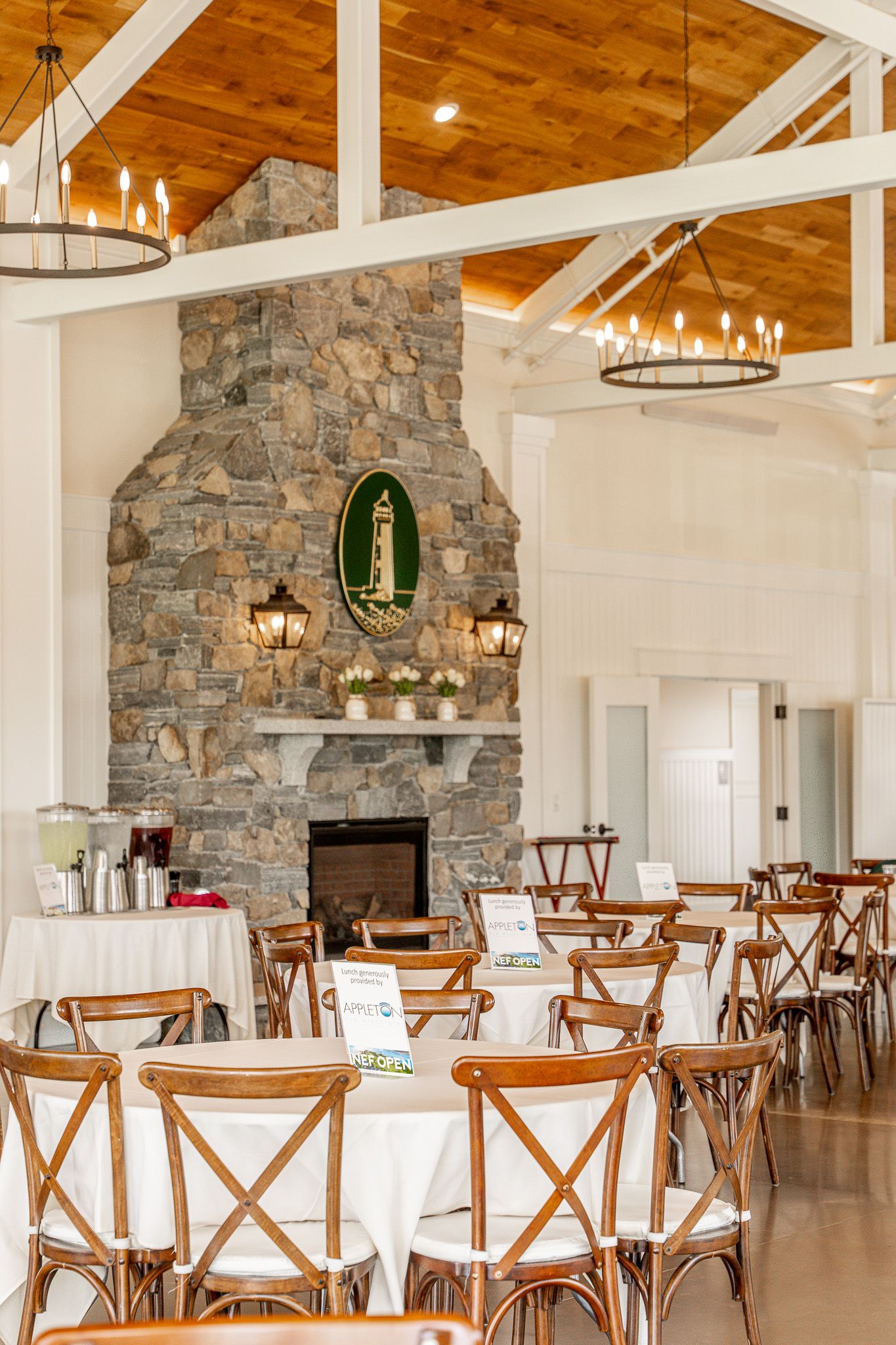Event photography of a table in front of a stone fireplace with chandeliers and exposed beam ceiling at Wentworth by the Sea Country Club.