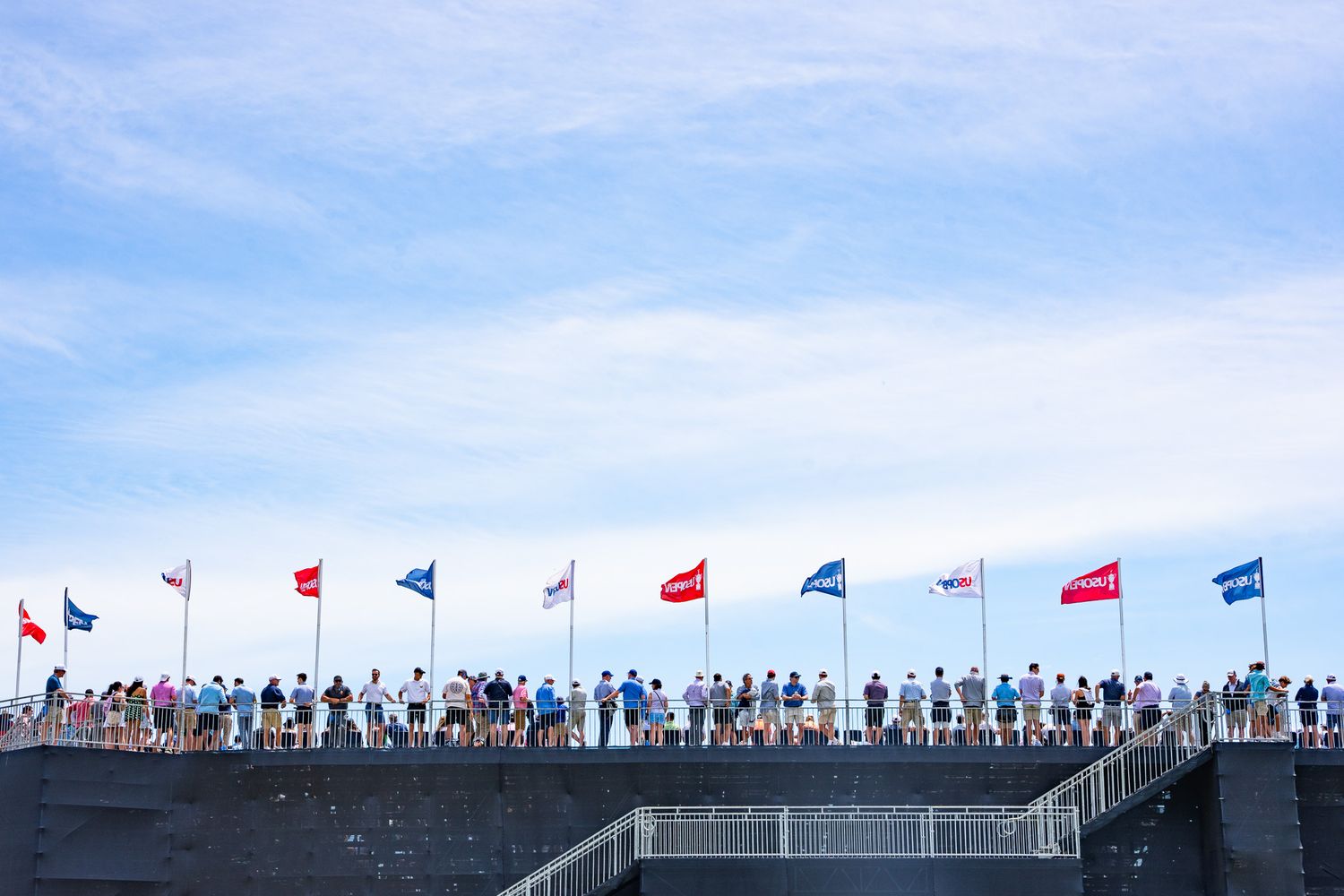 Event photography of a bright blue sky over the top of spectator stands with branded U.S. Open Flags waving at the Championship in New York