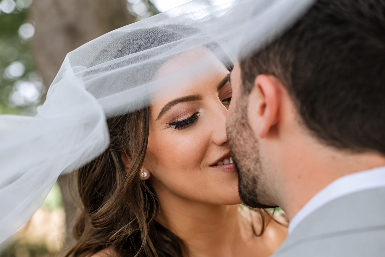 Bride kissing groom underneath wispy veil at their Summer wedding in Newburyport, Massachusetts