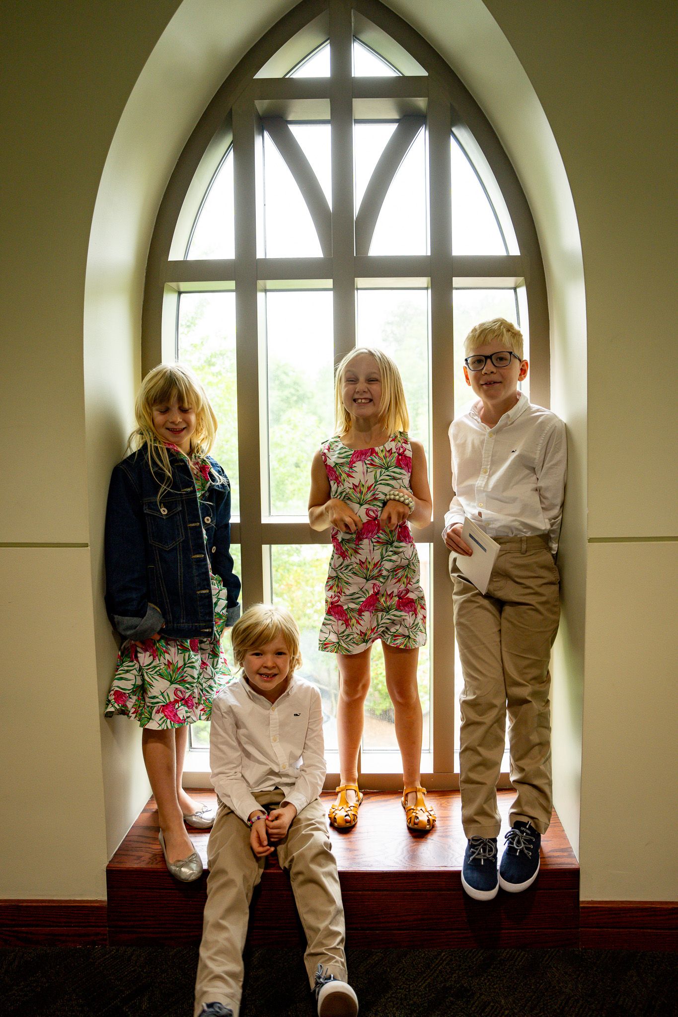 Family portrait of four blonde cousins, two boys and two girls, standing and sitting inside a tall church window during a Georgia wedding