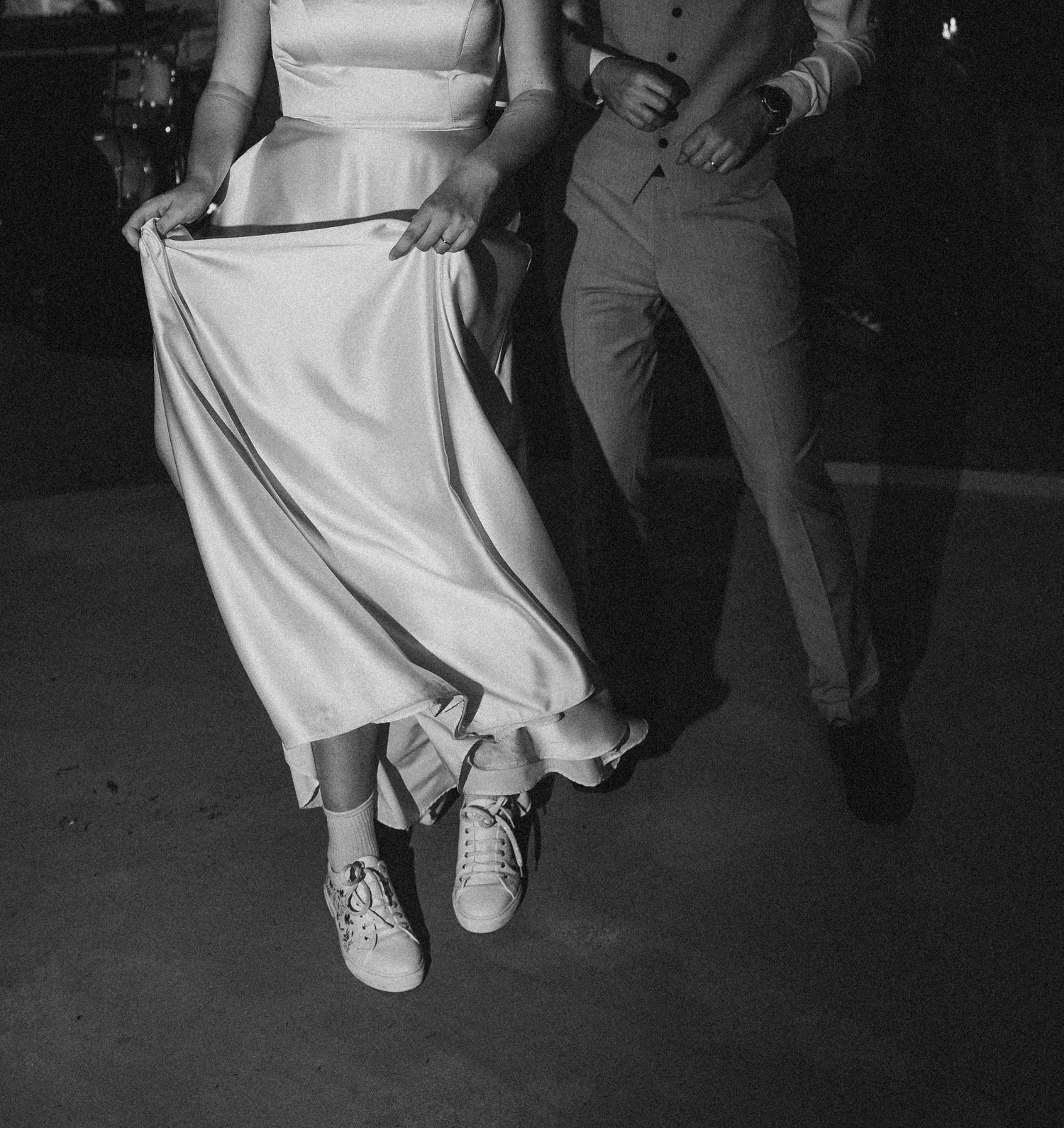 A bride lifts her elegant silk gown to show off her Converse sneakers while she dances at her wedding reception in Old Port Portland, Maine