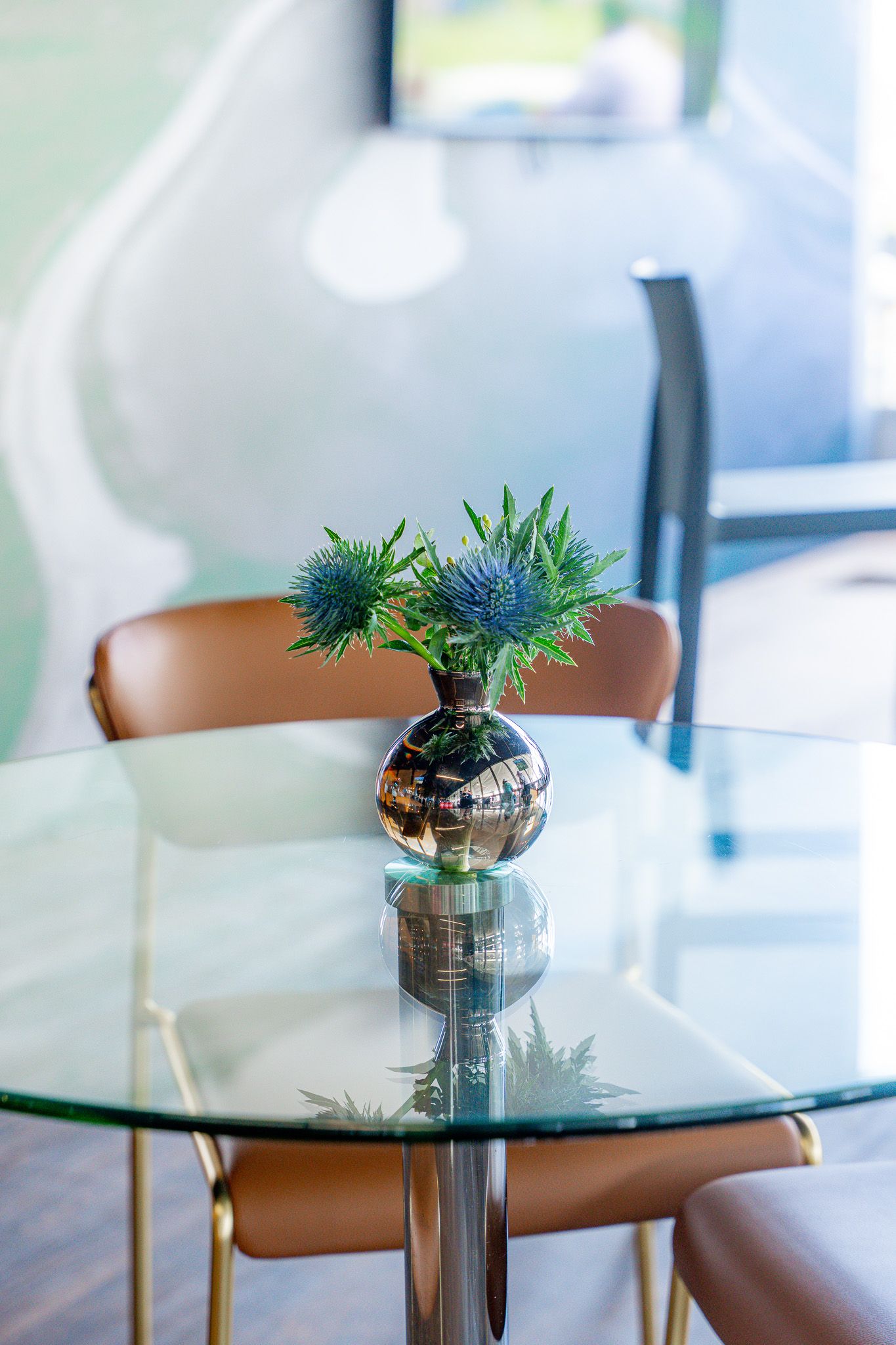 A glass table with a leather chair and green florals inside the 1895 Club at the U.S. Open Golf Championship in the Hamptons, New York