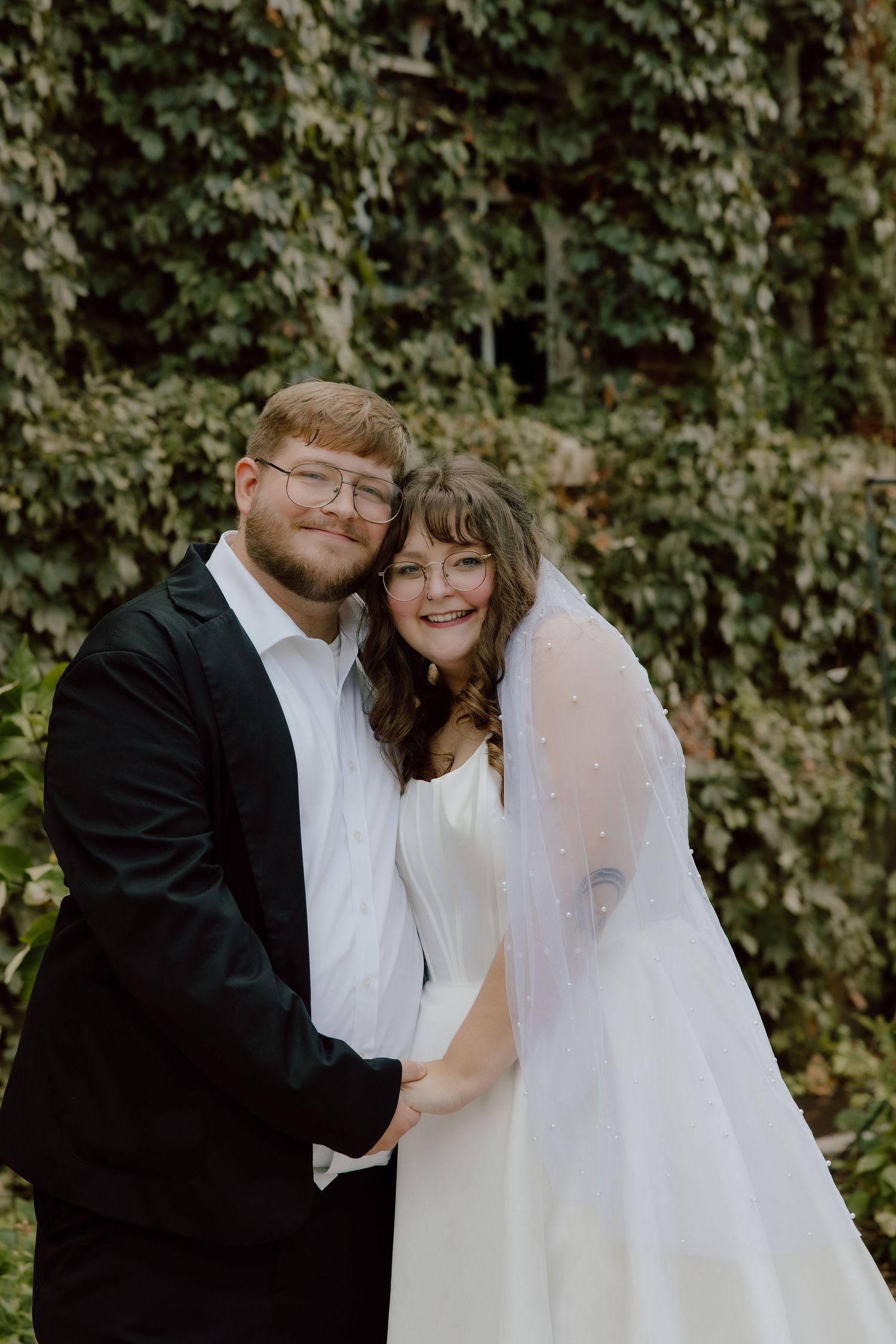 Formal bride and groom traditional portrait in front of greenery wall with a true to color photograph.