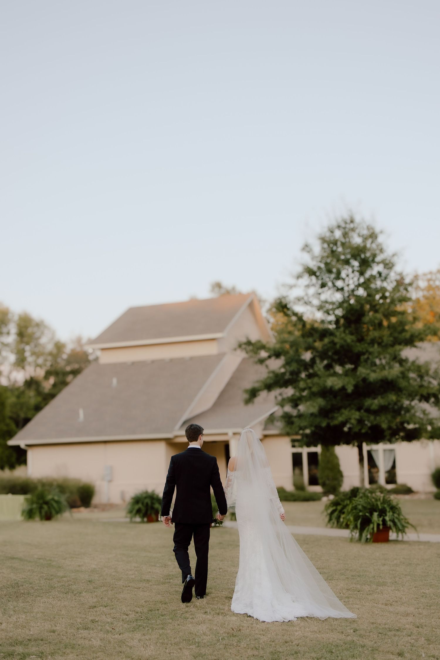Documentary wedding photographer capturing candid couple moment of bride and groom walking towards The Loft at Stone Oak venue in Arkansas.