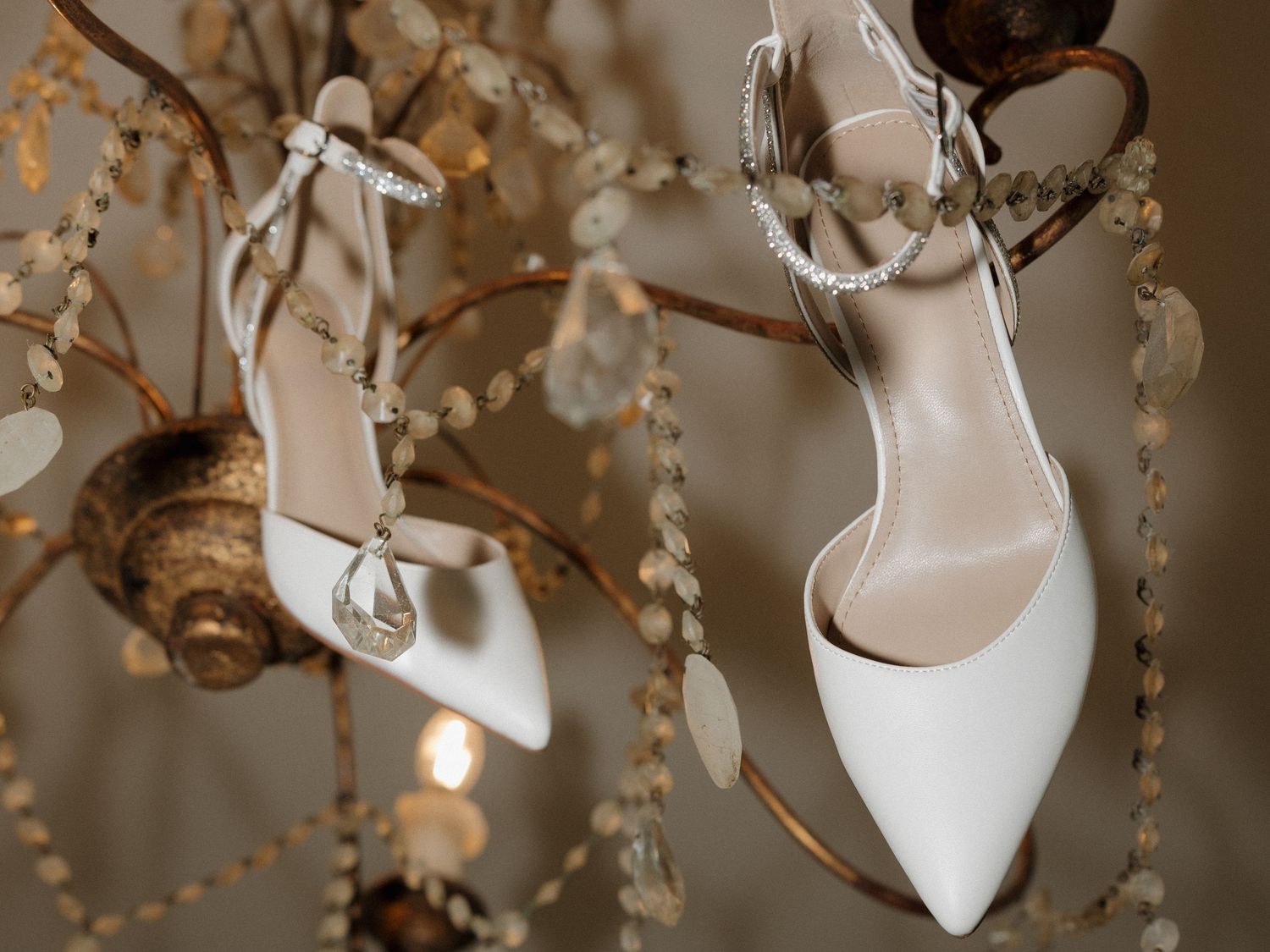 Brides white wedding shoes hanging in the chandelier of their getting ready room before wedding.