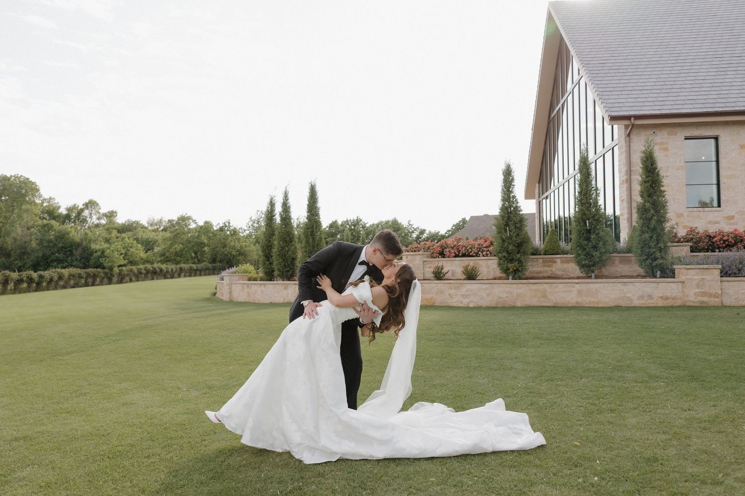 Groom dipping the bride into a kiss in front of The Bower wedding venue.