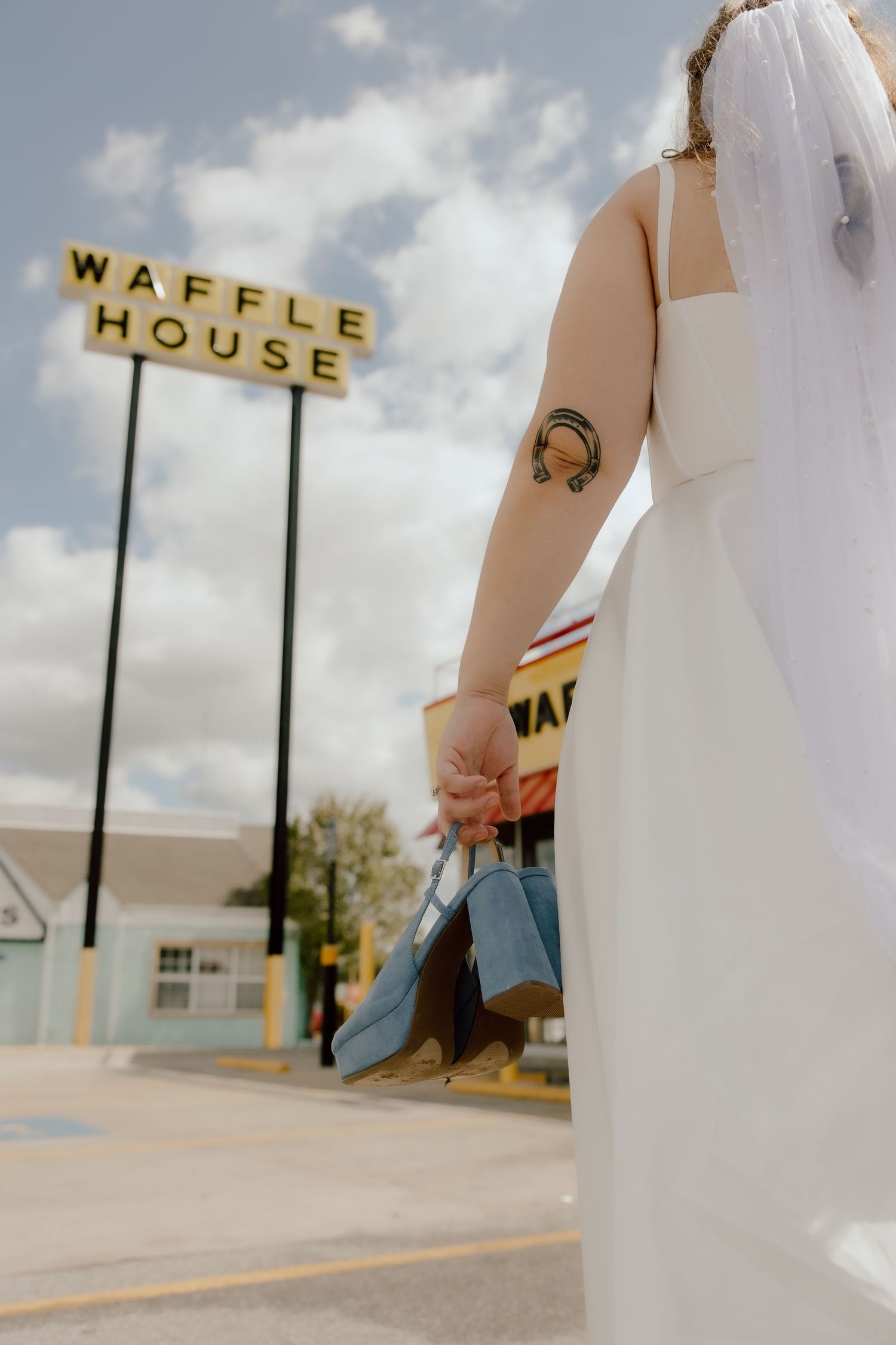 Editorial direct sunlight style photo of bride carrying her blue wedding shoes into Waffle House in Fayetteville, Arkansas after eloping.