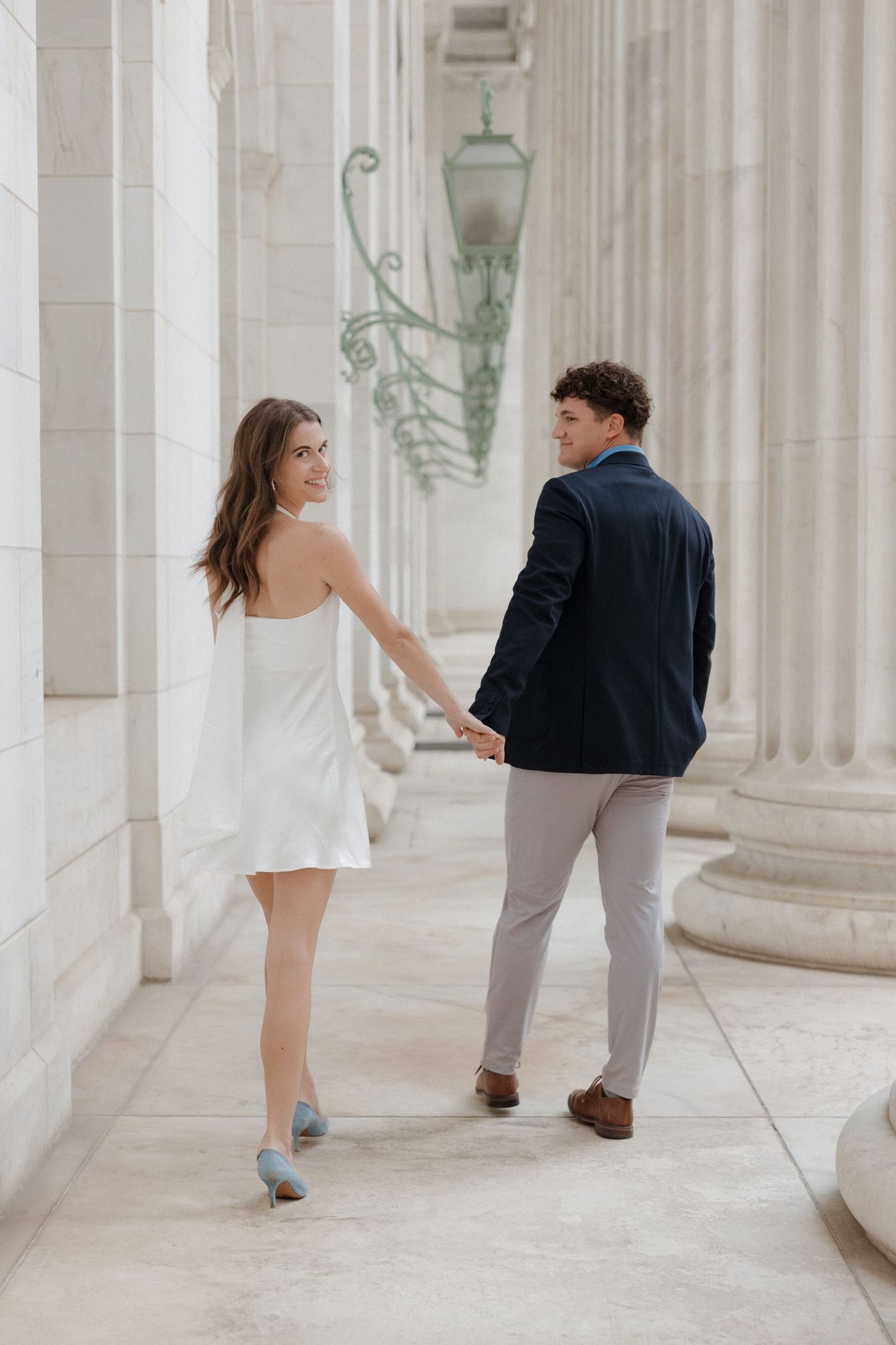 Candid moment of couple laughing and spinning in front of the white stone columns of Byron White Courthouse in downtown Denver