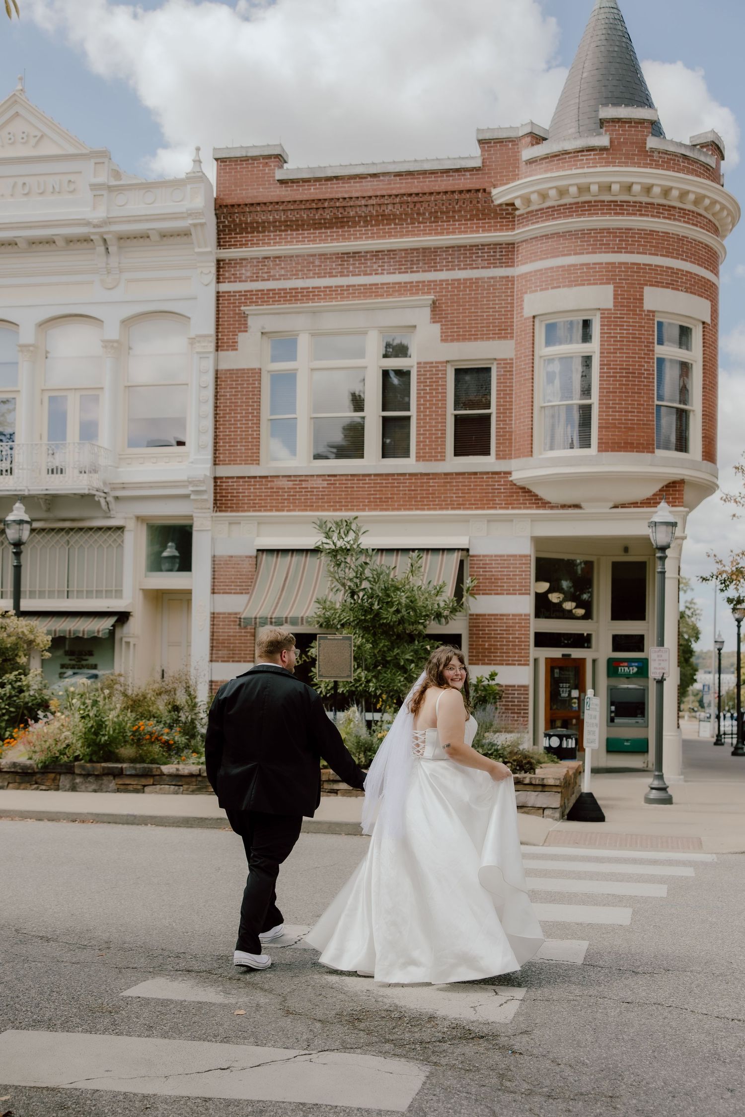 Bride and groom walking across a crosswalk on a bright sunny summer day at the downtown square area of Fayetteville, Arkansas.