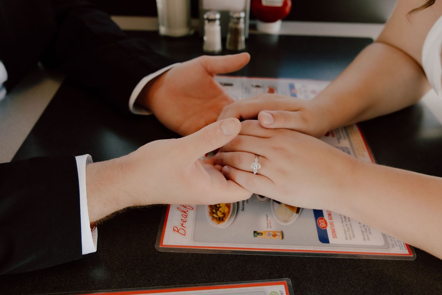 Documentary detail photo of bride and grooms hands with rings on top of the menu at Waffle House after getting married earlier that day.