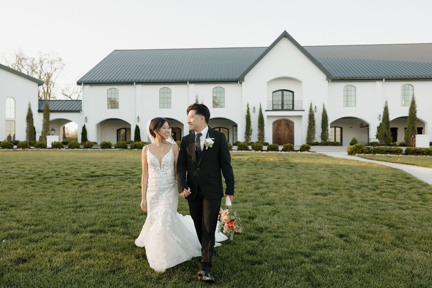 Bride and groom walking hand in hand in front of The Grand at Willow Springs wedding venue in Prairie Grove.