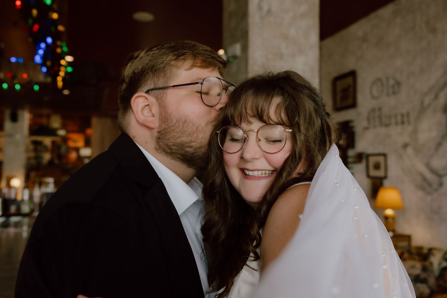 Groom kissing the brides head in a sweet romantic moment at the Graduate Hotel bar in NWA.