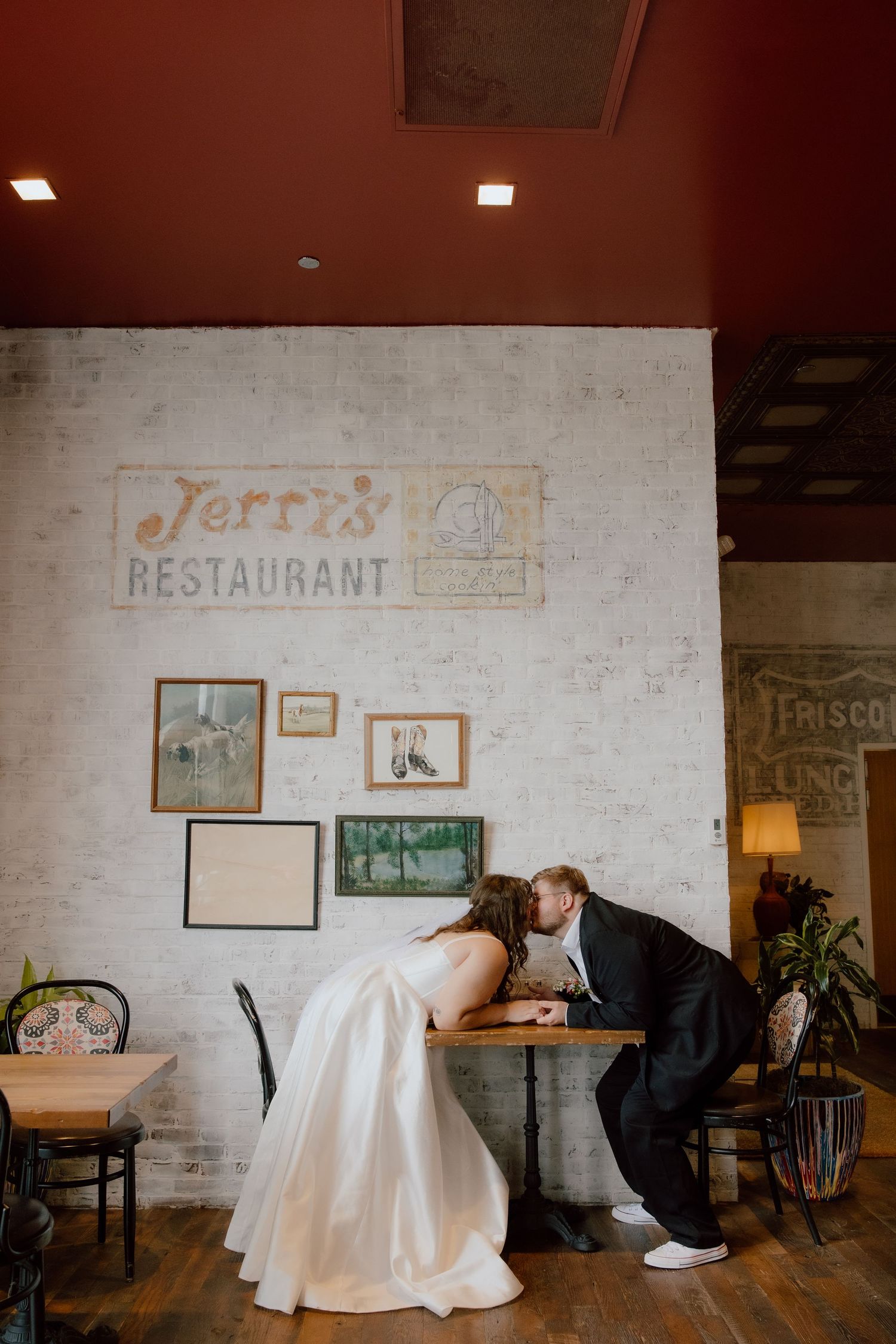 Bride and groom kissing across a table and holding hands in the bar area of The Graduate Hotel before sharing wedding cake!