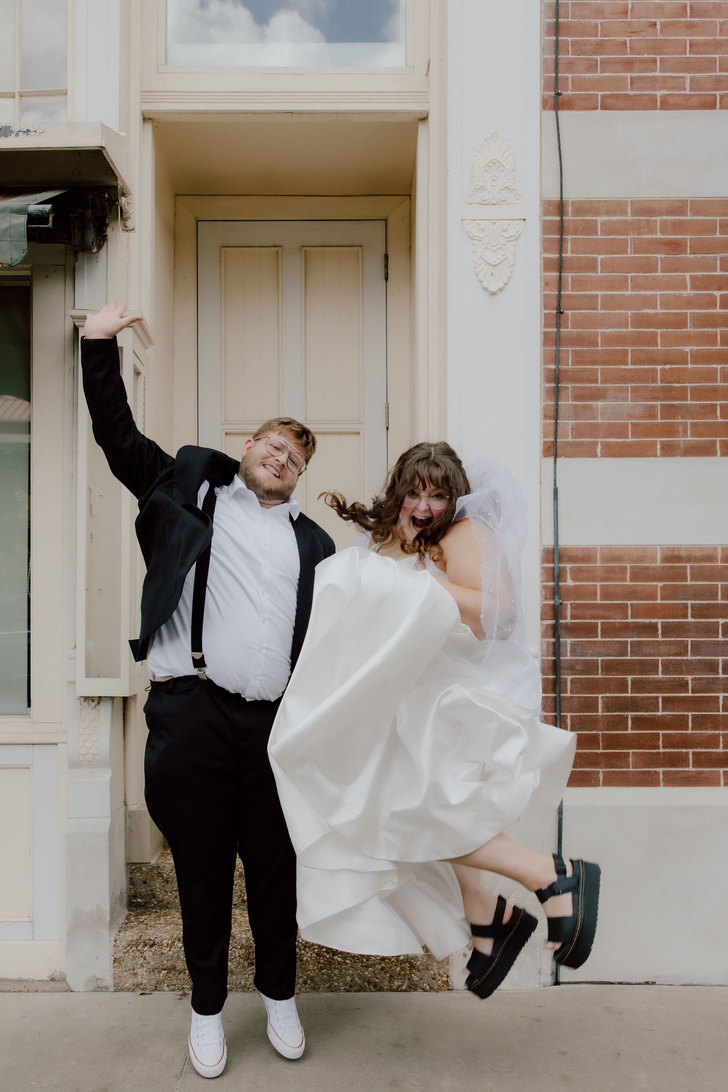Fun, candid, emotive bride and groom couple portrait of them jumping in the air with joy in front of local Fayetteville businesses.