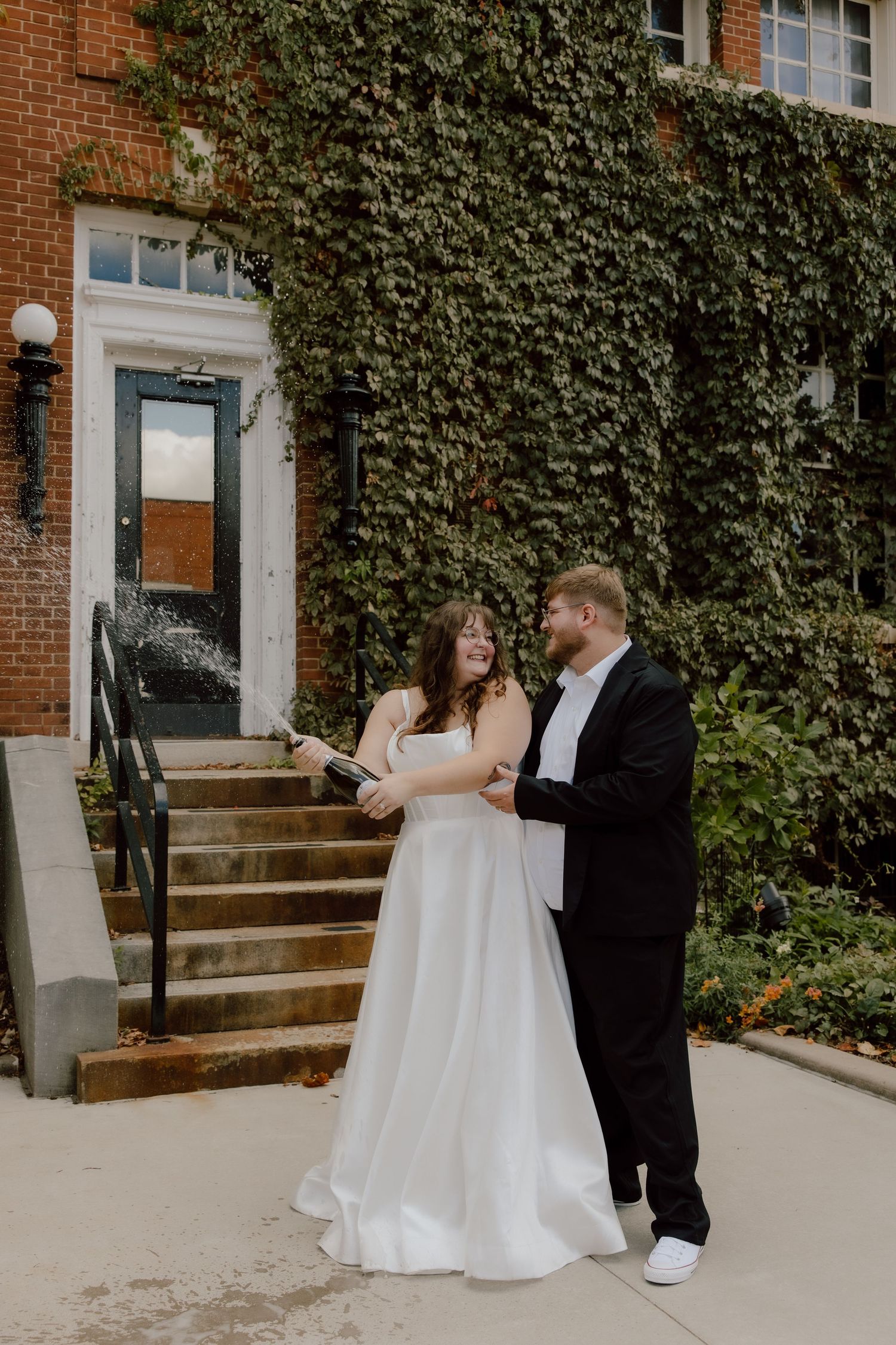 Bride and groom celebrate their recent elopement by spewing a bottle of champagne celebrating in a candid moment.
