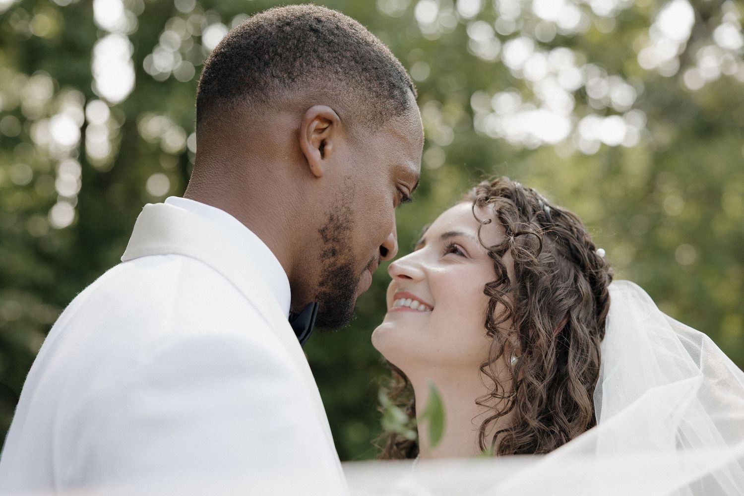 Bride and groom are featured in a sweeping veil moment. Faces close and looking at each other lovingly during portraits.