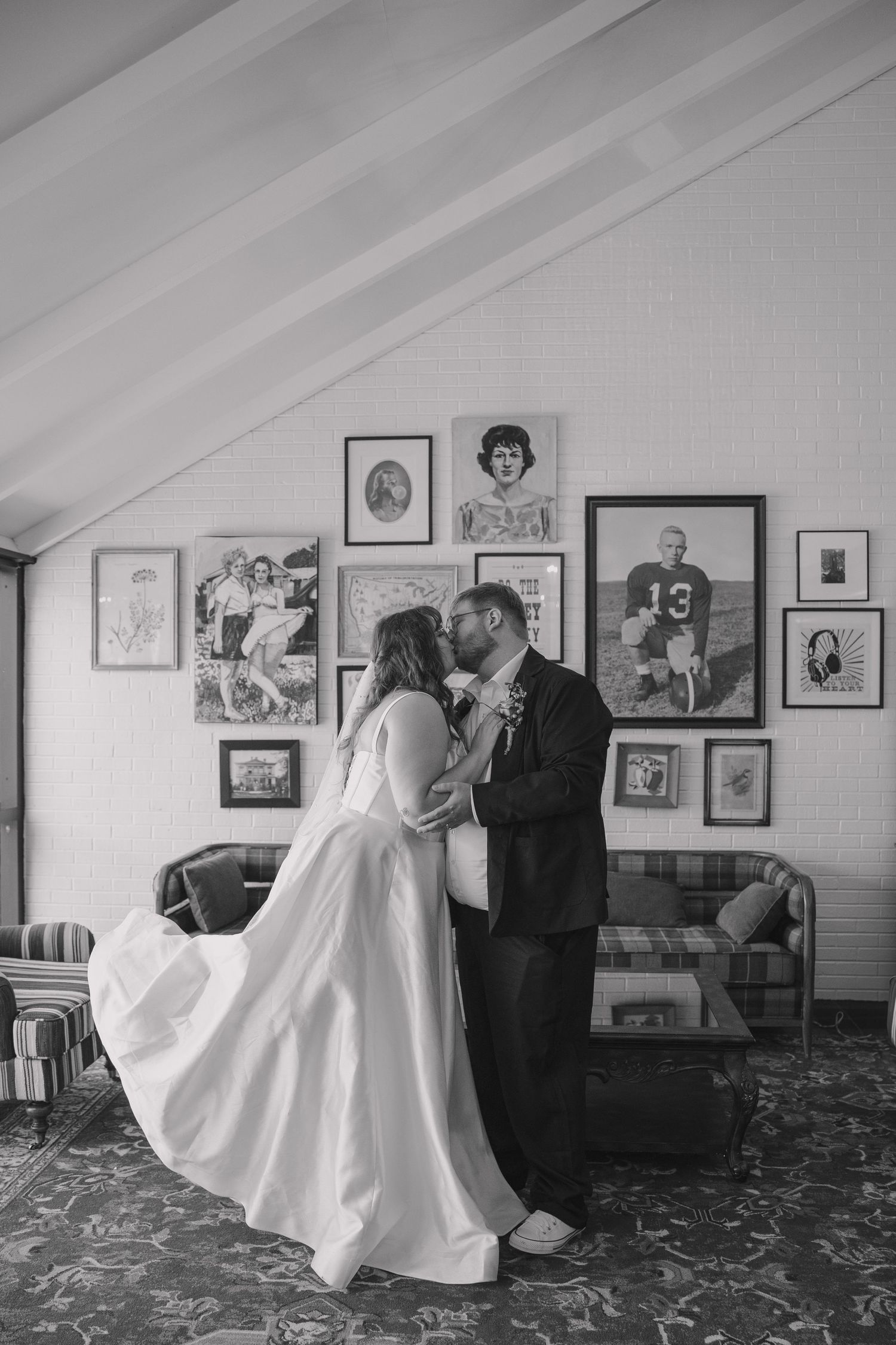 The Graduate Hotel art gallery wall serving at the background for this romantic wedding day portrait of first kiss in black and white.