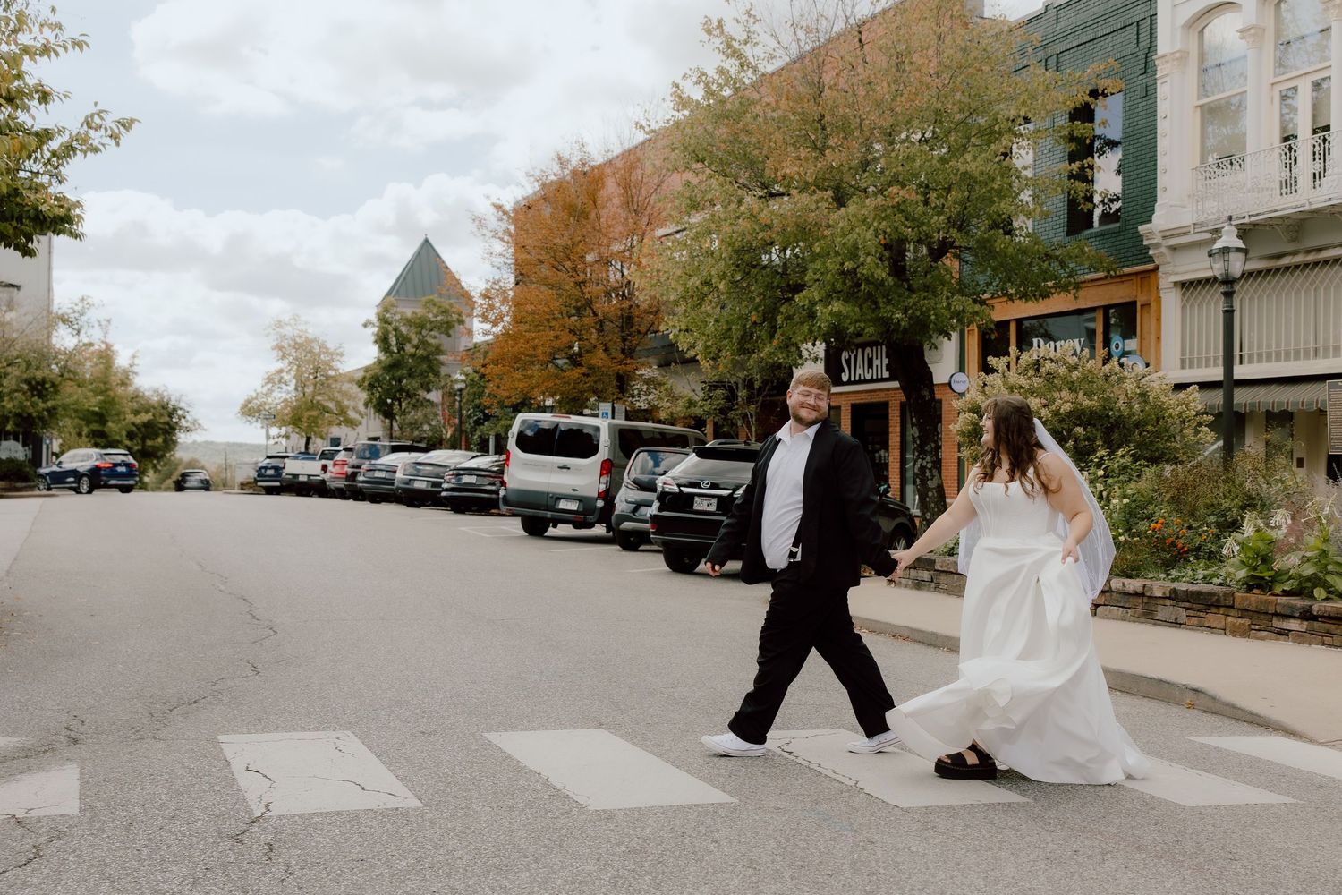 Documentary style photograph of bride and groom walking in downtown Fayetteville across a crosswalk on a fall day.