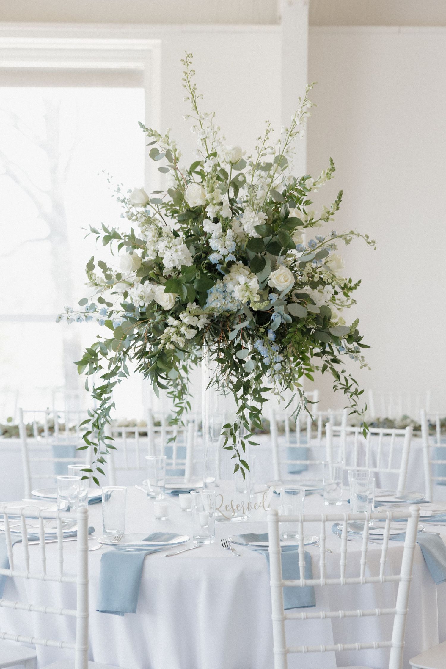 White, blue, and green floral arrangement placed on white tables for reception at Cold Springs Events wedding venue.