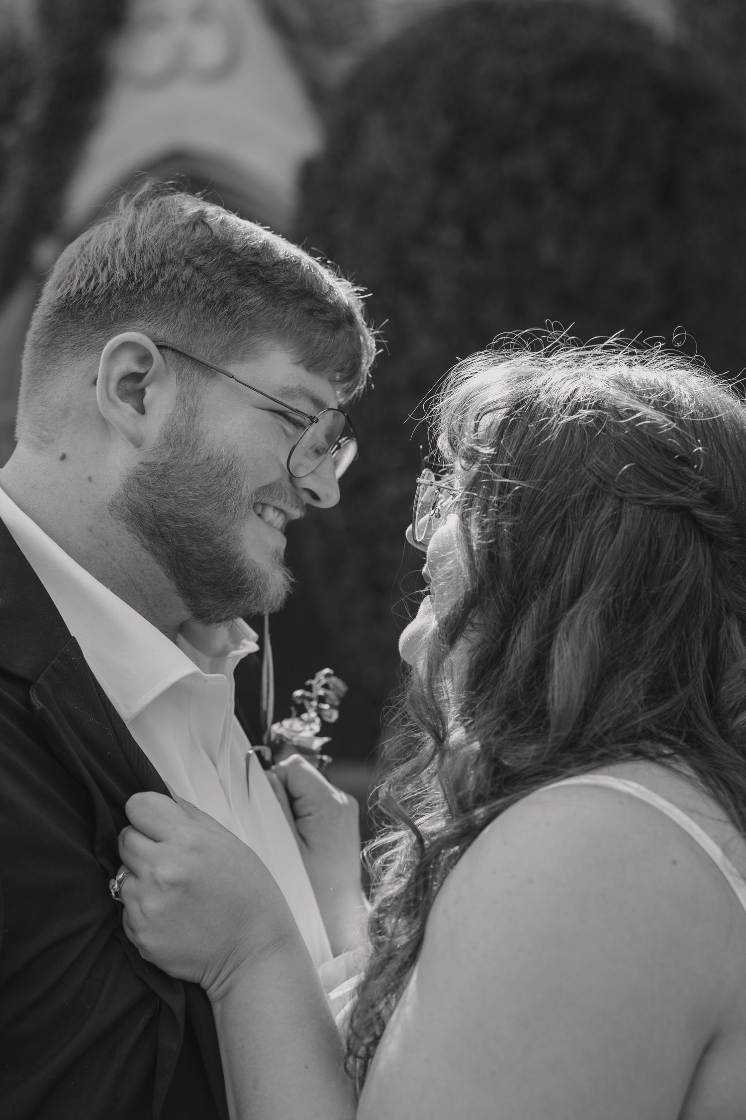 Bride and groom in intimate pose of her holding on to his suit with the direct sunlight shining on them with their wedding venue in the back