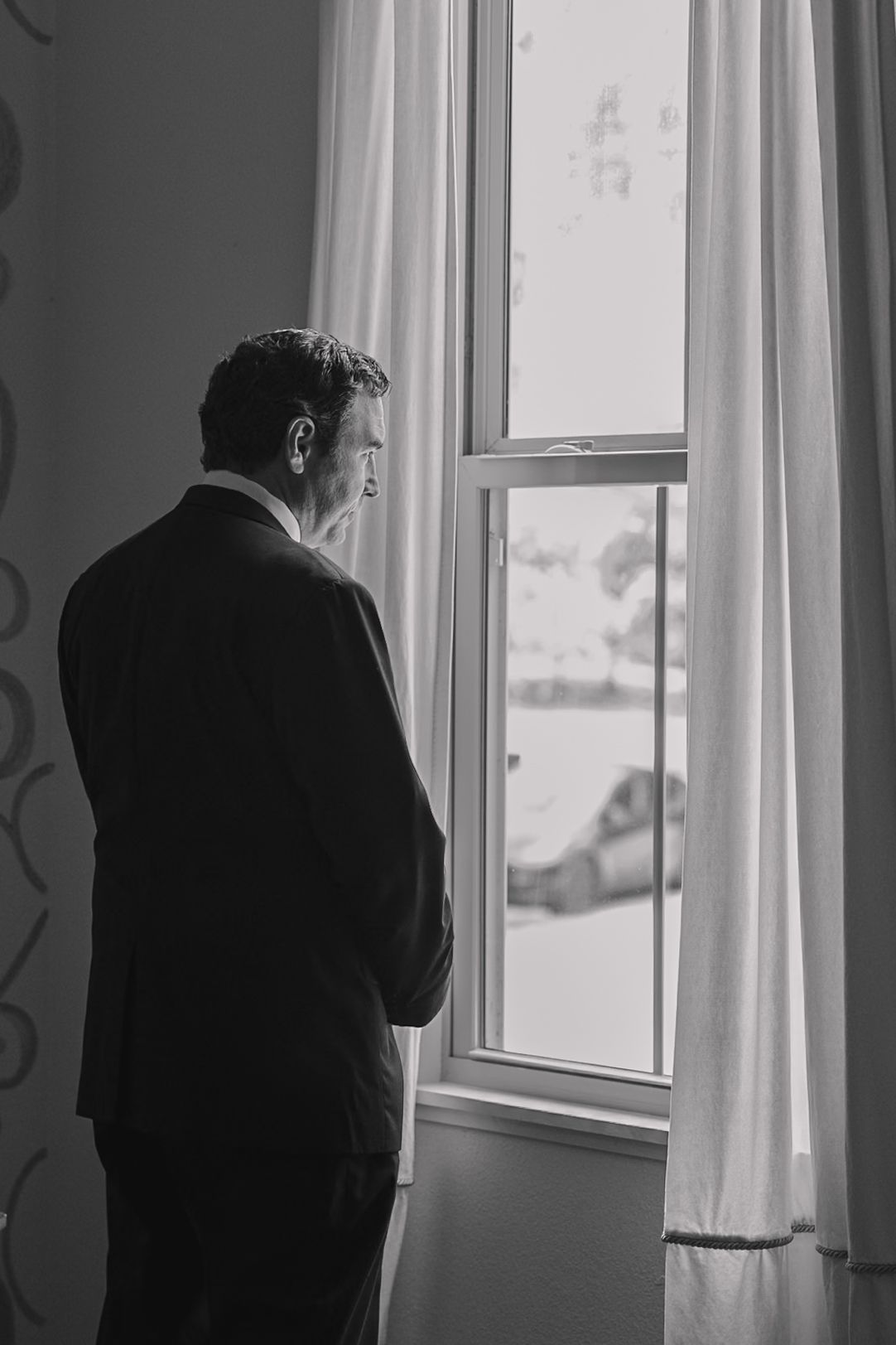 Father of the bride is looking out the window before the wedding ceremony of his daughter.